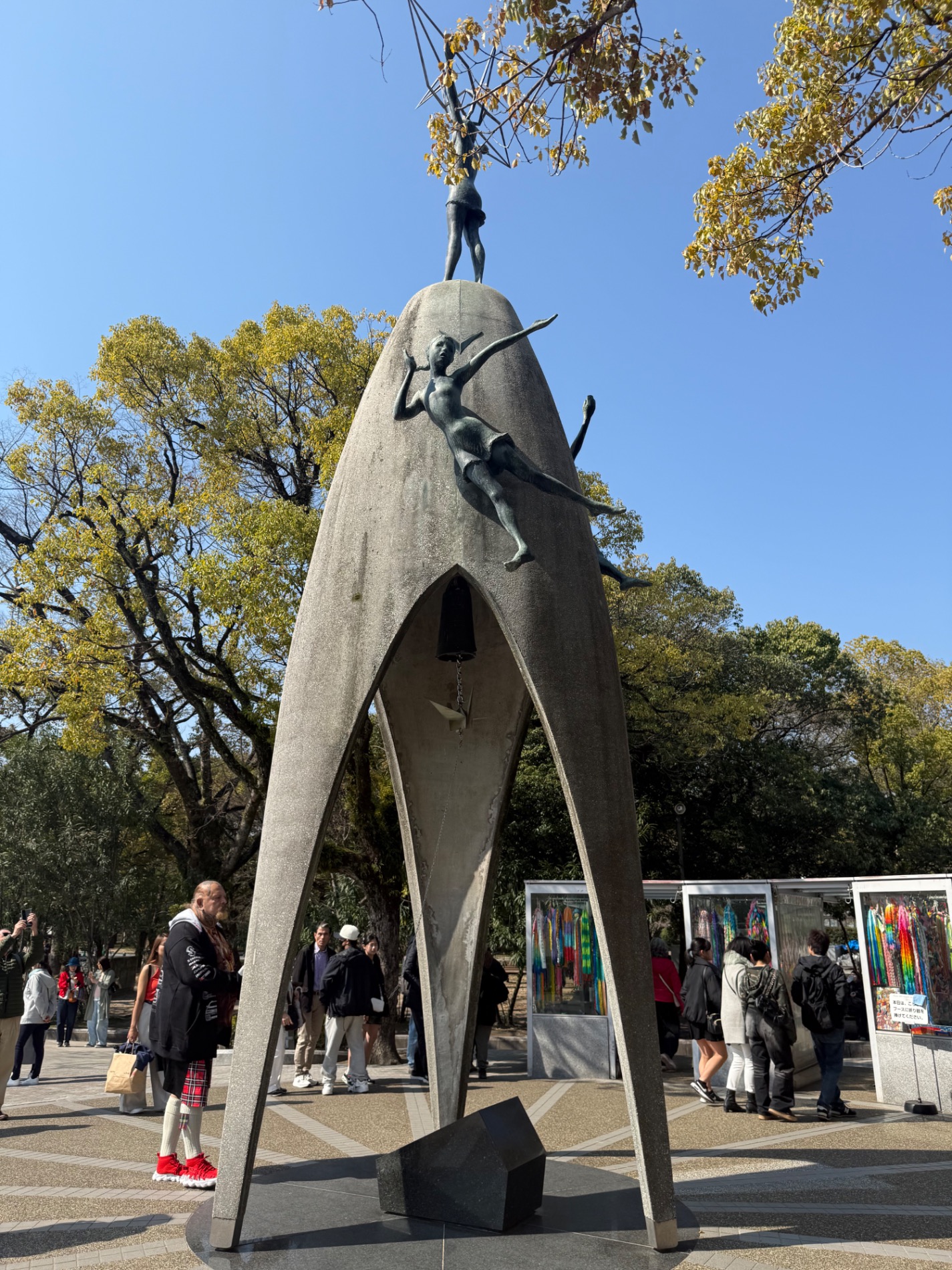 Man and woman posing at a peace memorial site with a distinctive sculptural monument in Hiroshima