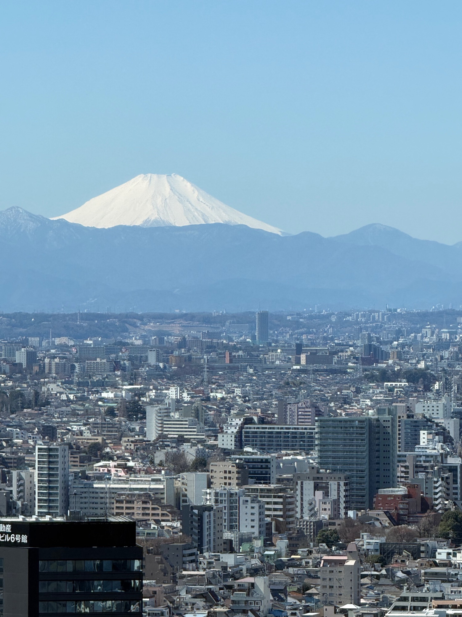 Mount Fuji snow-capped peak rising above a sprawling Japanese city under clear blue sky