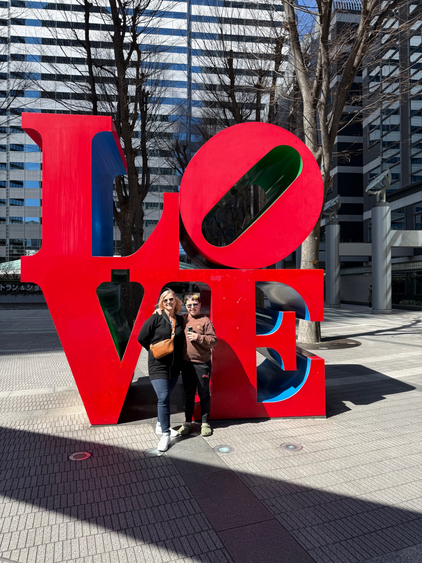 Woman and man standing in front of a large red LOVE sculpture in an urban plaza with bare trees