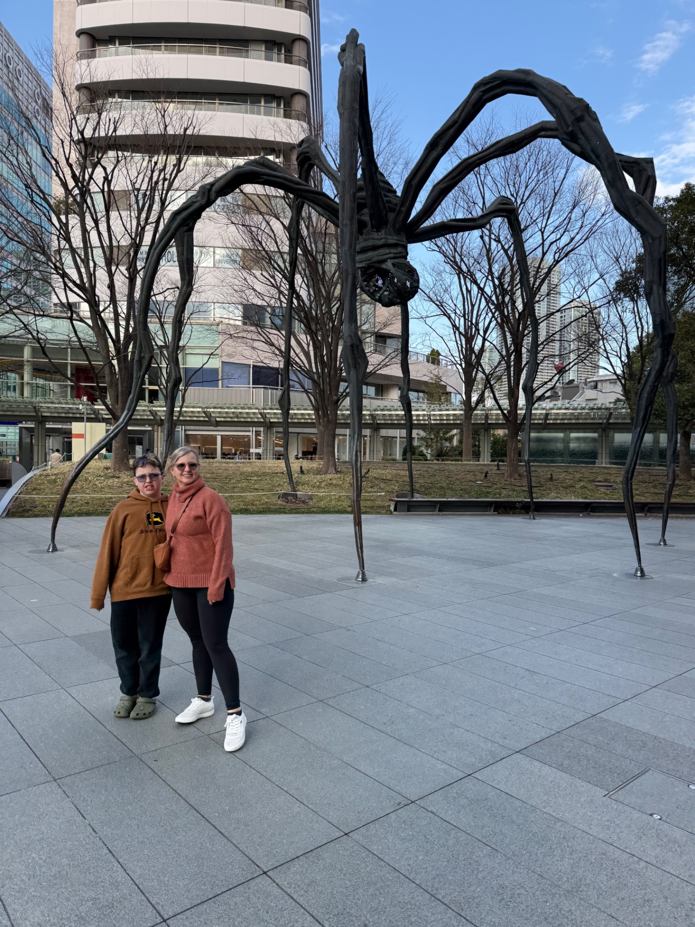 Woman and young boy posing with a large black spider sculpture in an urban courtyard setting