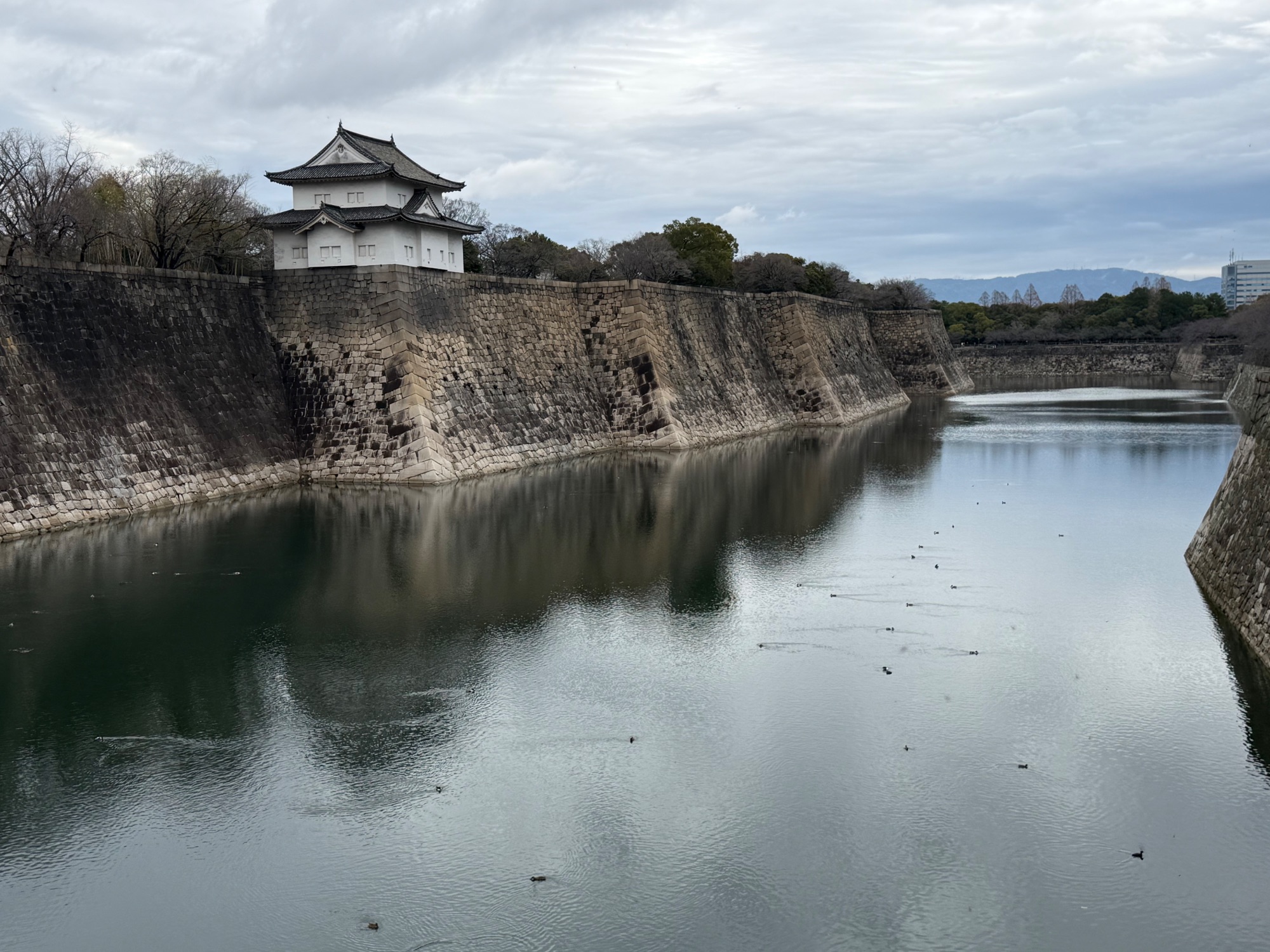 Historic Japanese castle with white walls and green roof reflected in still water surrounded by stone walls