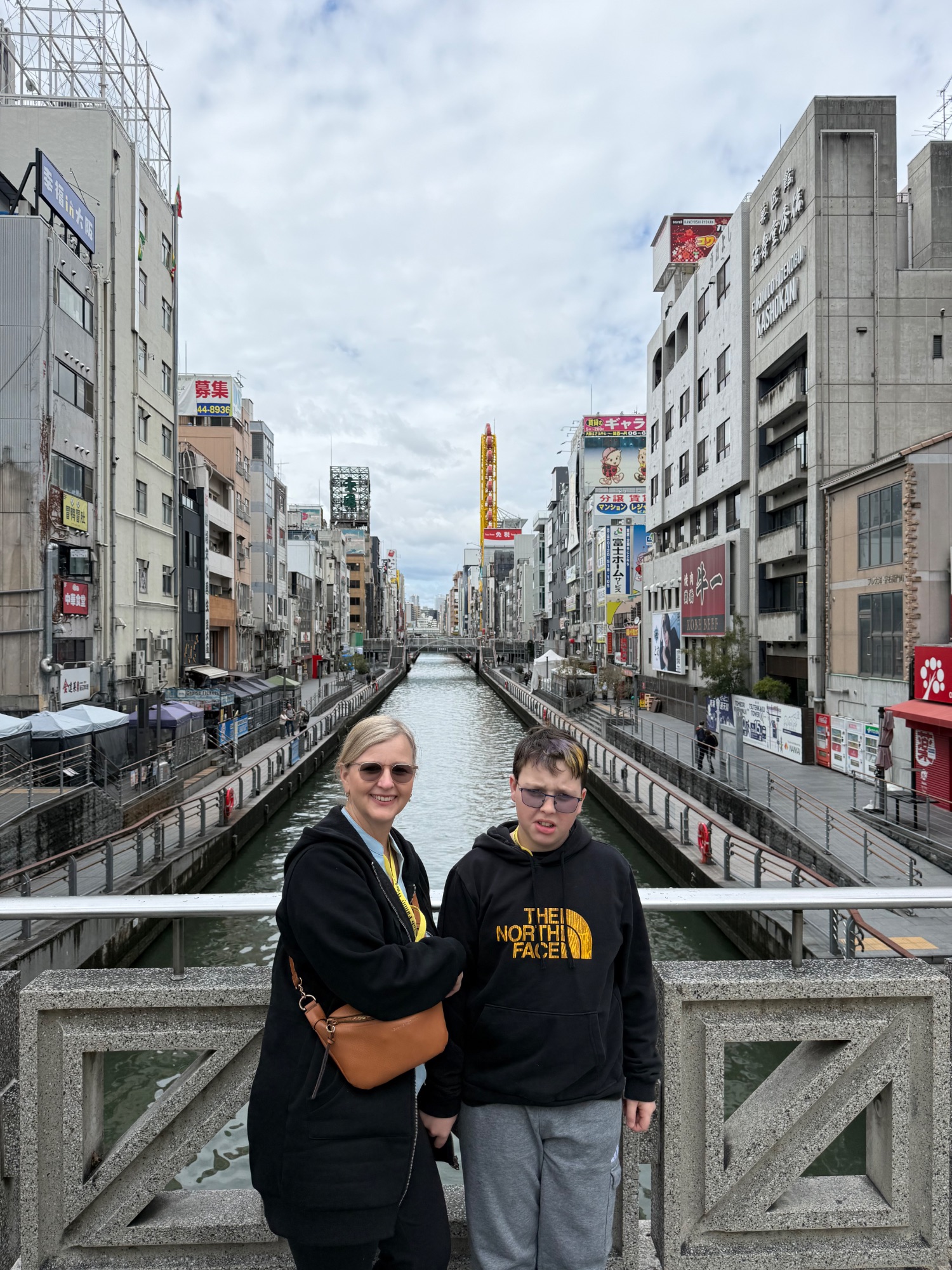 Woman and boy on a bridge overlooking a canal lined with shops and signs in a Japanese shopping district