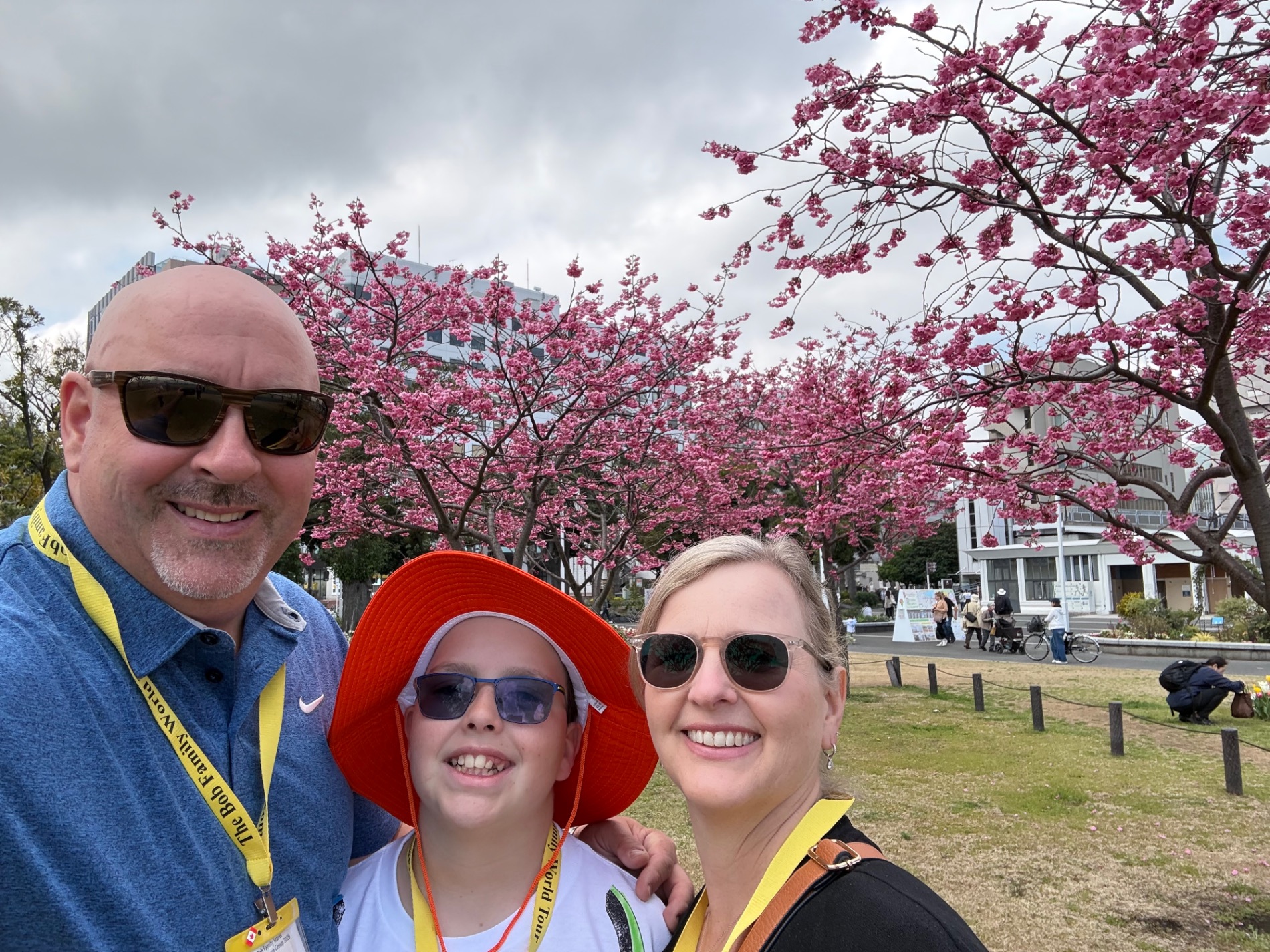 Family of three in spring clothing with blooming pink flowers in background at a Japanese park