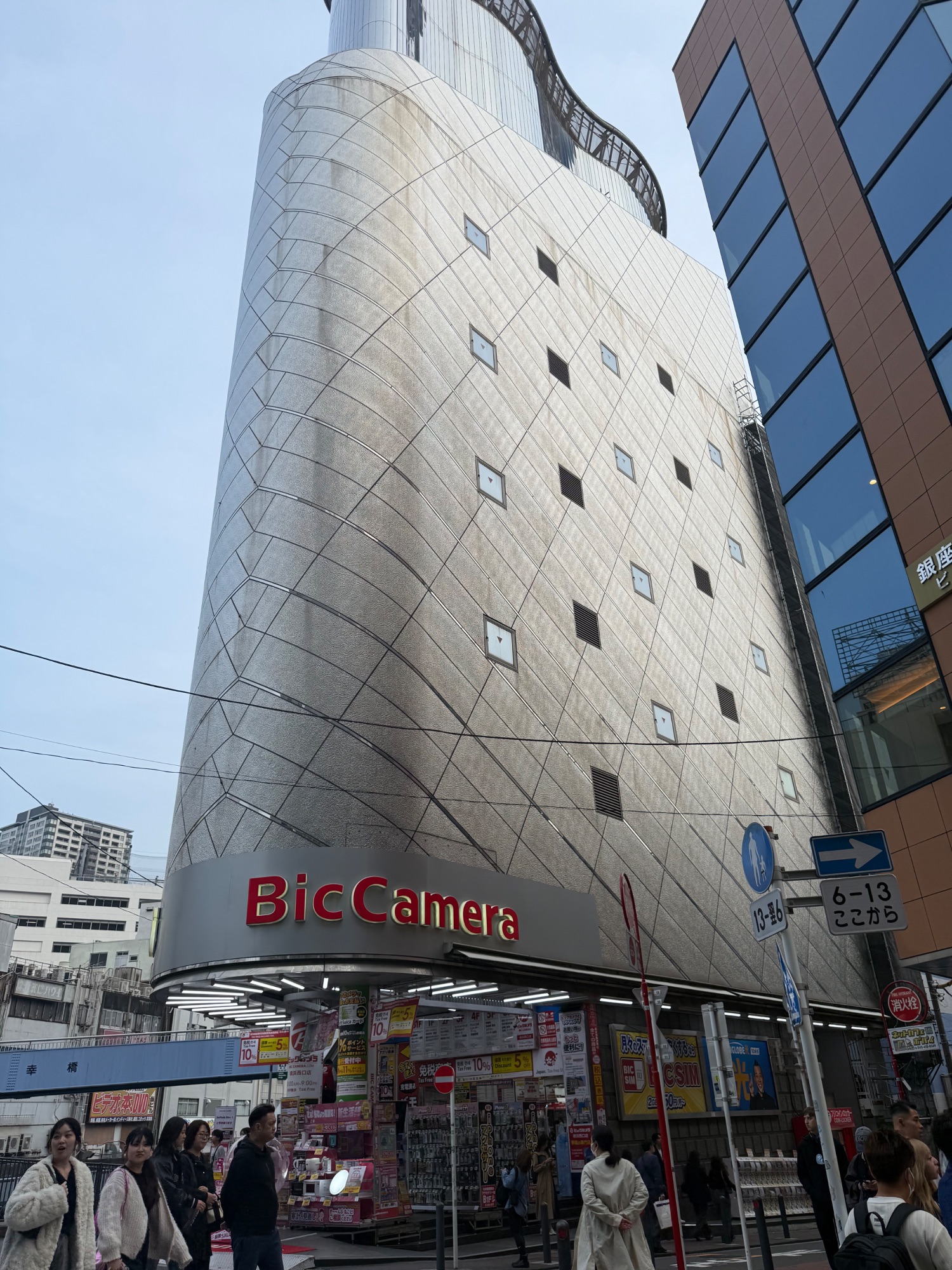 Tall cylindrical building with BicCamera signage at street level in a Japanese urban shopping area