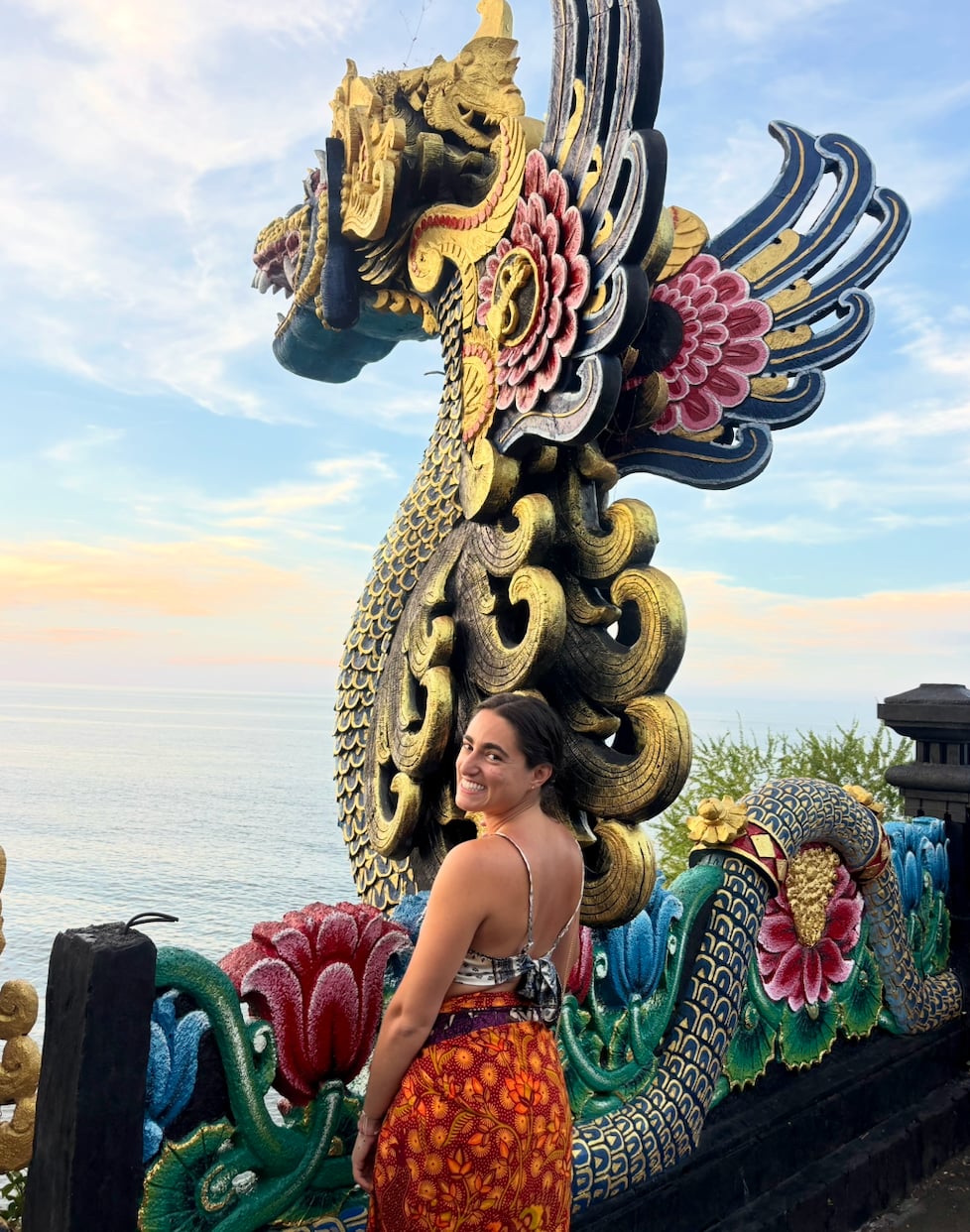 Julia Cianci poses beside an ornate golden dragon statue overlooking the ocean in Bali