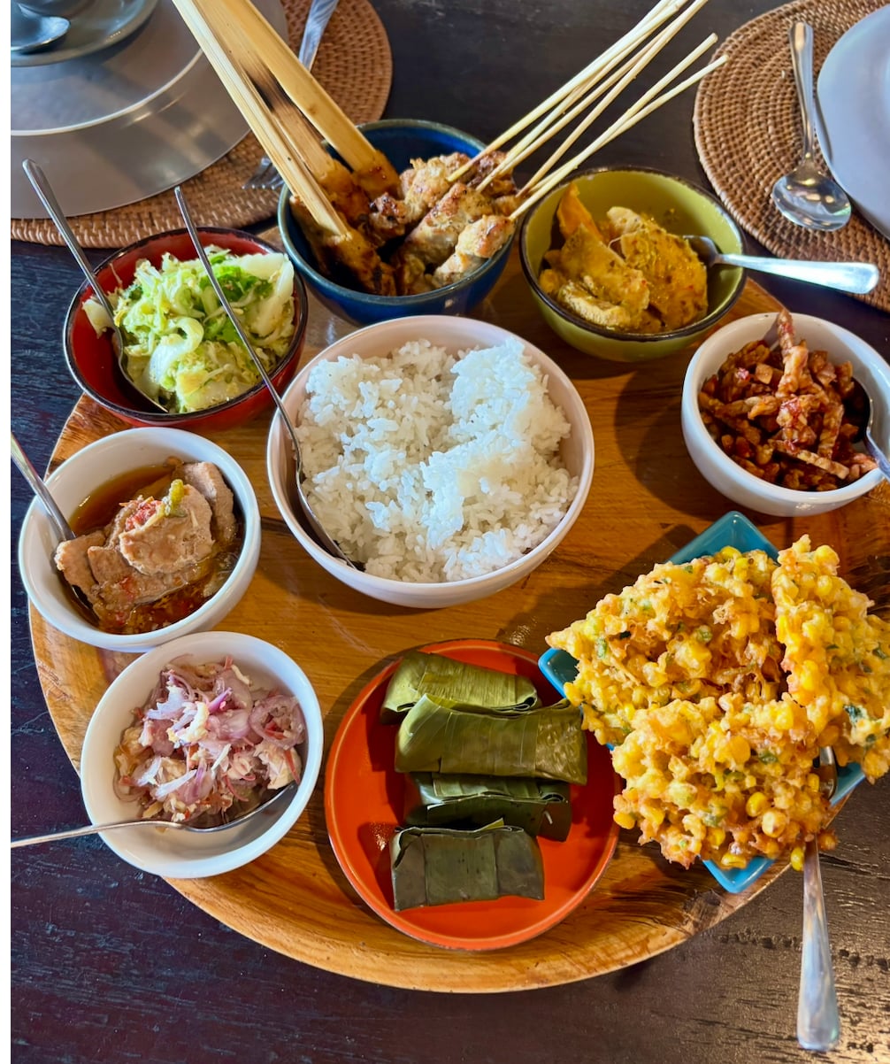 Overhead shot of a traditional Balinese meal with rice, satay skewers, curry, and vegetable dishes on wooden table