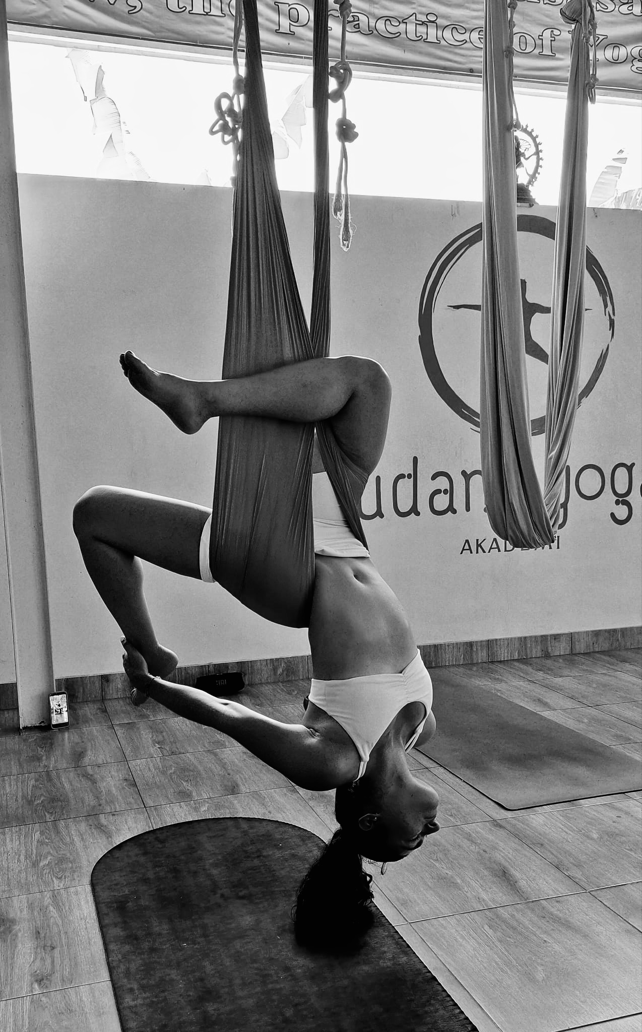 Person performing an inverted aerial yoga pose suspended in fabric straps in a studio setting