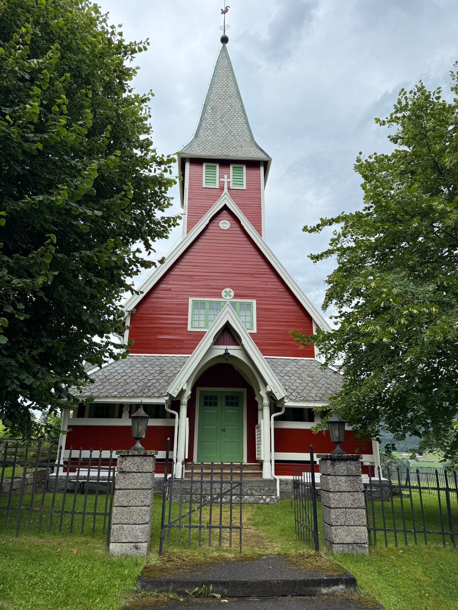 A gravestone with a golden cross and text in Norwegian, decorated with bright pink flowers