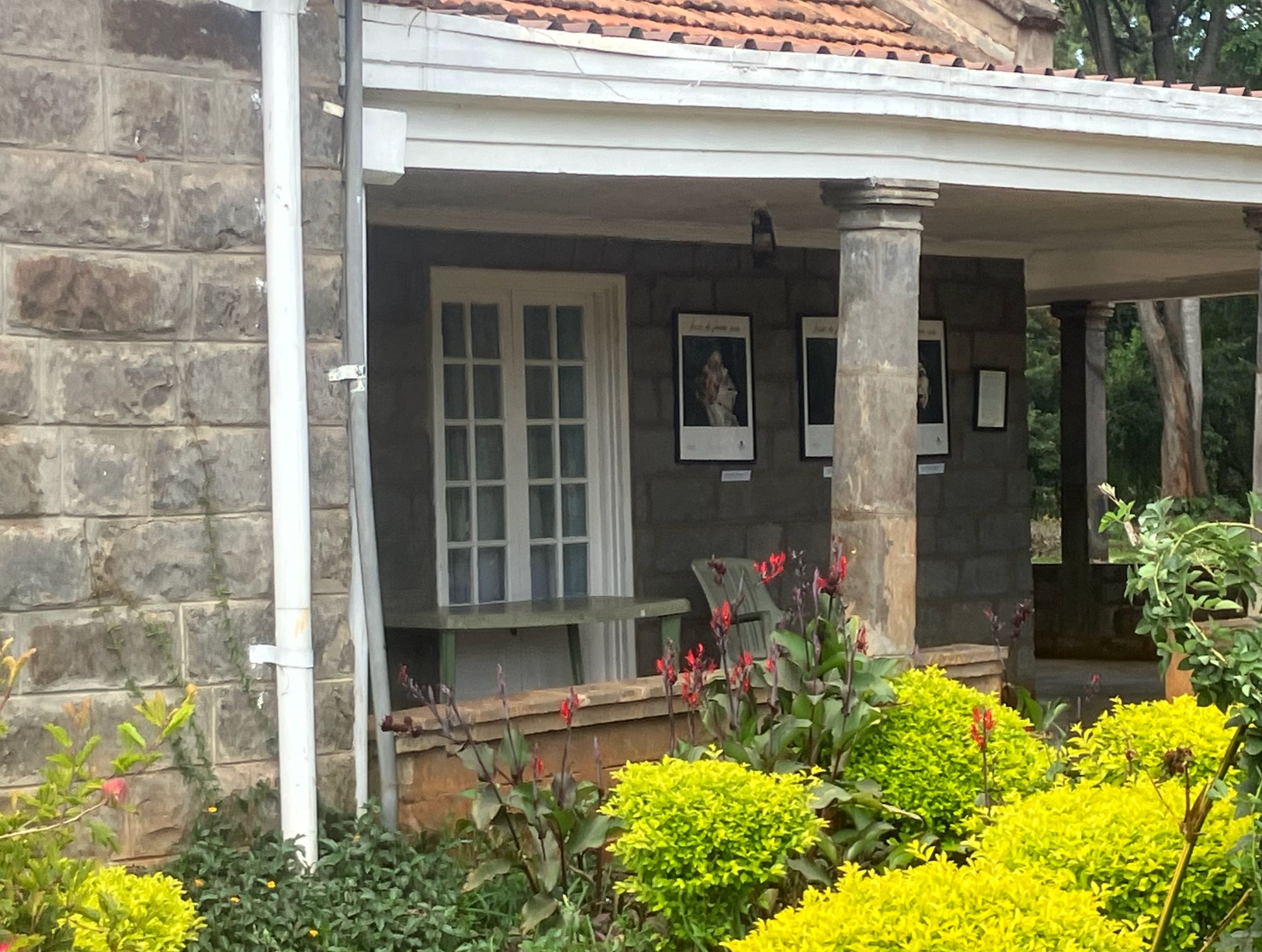 Stone cottage with white trim and red flowers in garden, part of Karen Blixen Museum in Kenya