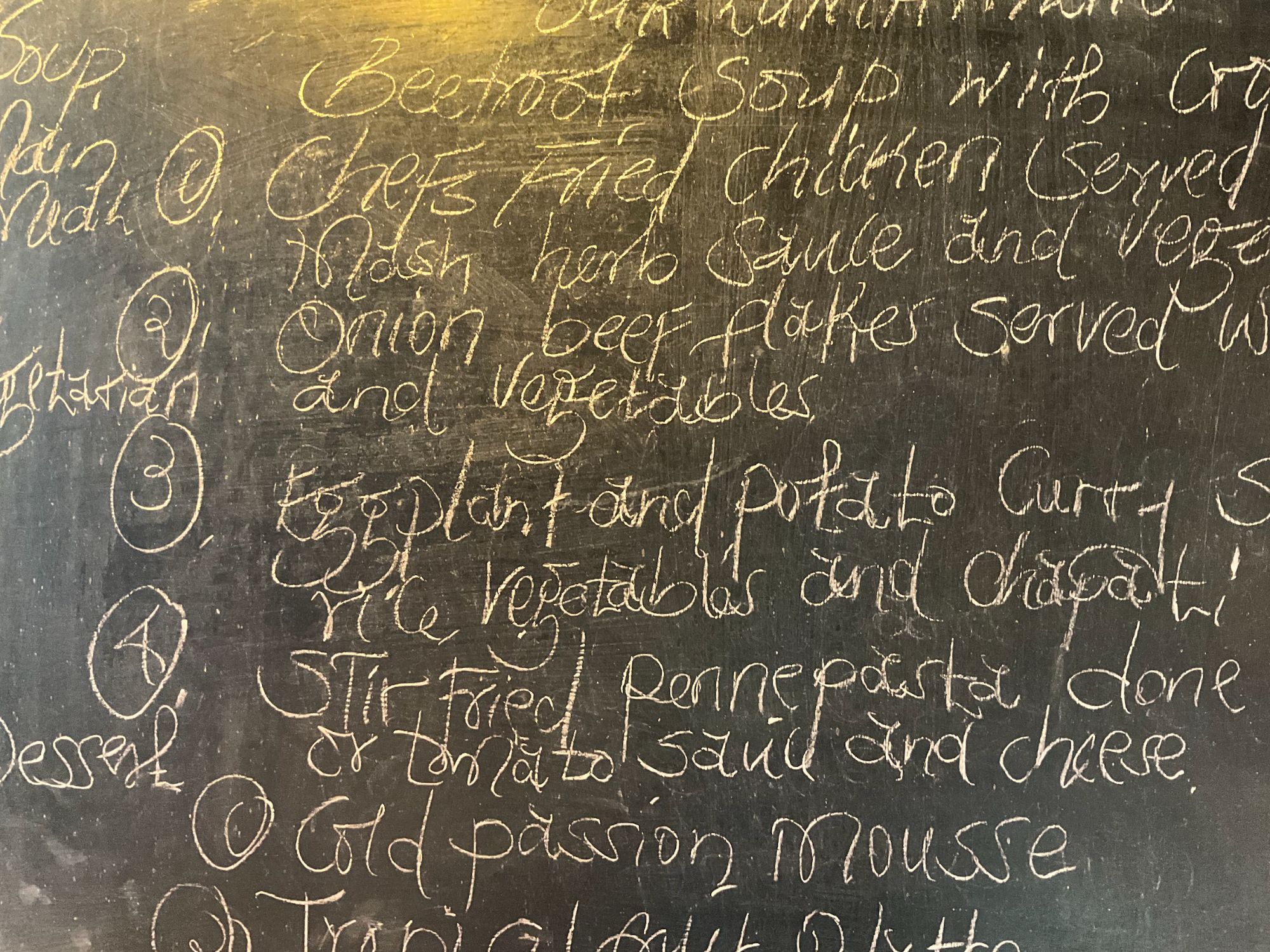 Handwritten menu on chalkboard listing traditional Kenyan dishes including game and vegetables