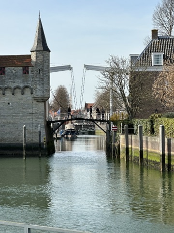 Stone tower and drawbridge spanning a calm waterway lined with wooden posts in rural Netherlands