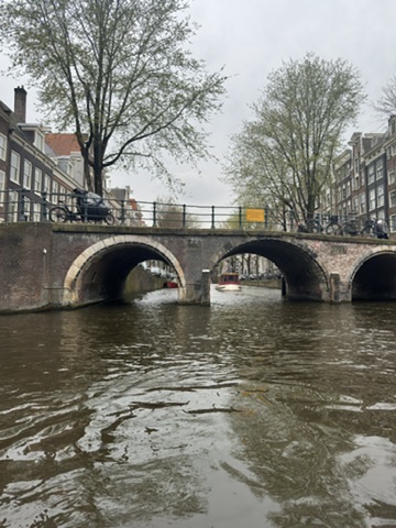 Stone arch bridge spanning an Amsterdam canal with historic buildings and bare trees along the bank