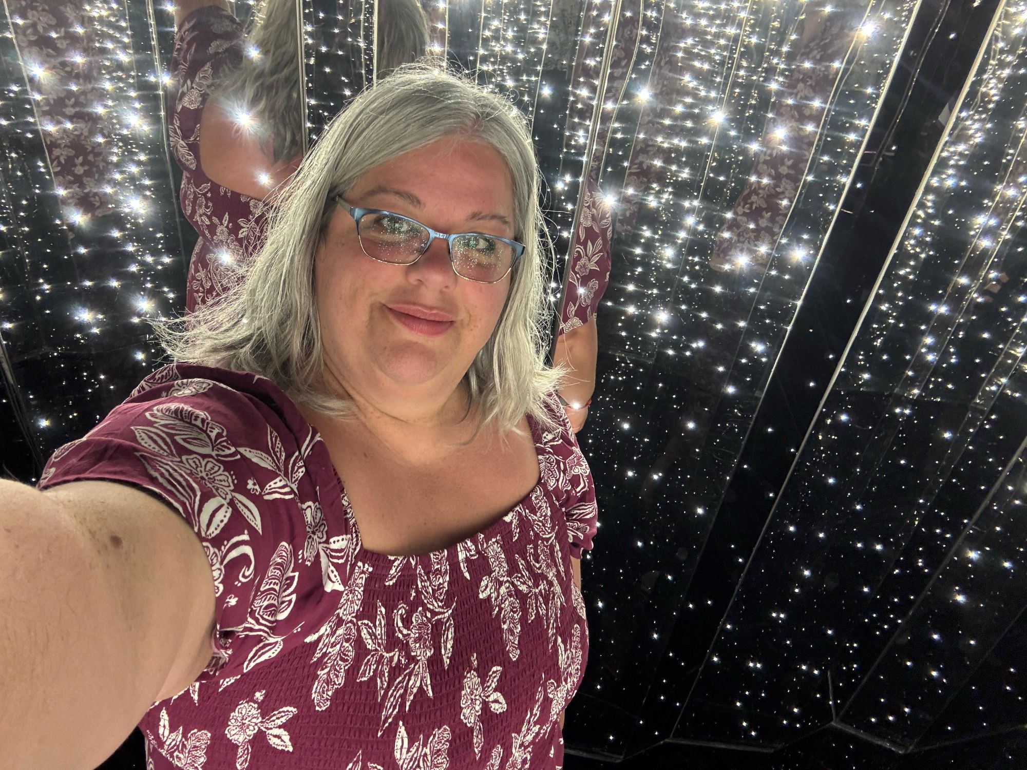 A woman takes a selfie inside a dazzling infinity mirror light installation exhibit.