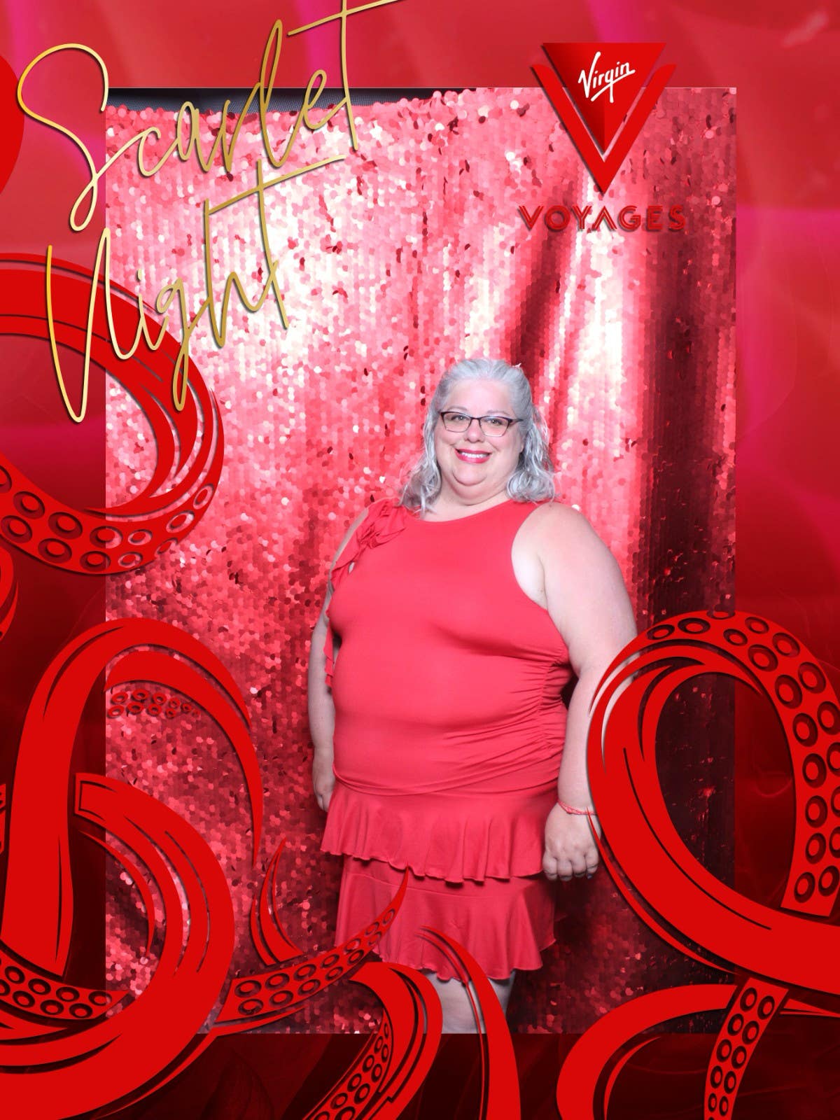 A smiling woman in a coral dress poses at Virgin Voyages' Scarlet Night themed photo booth.