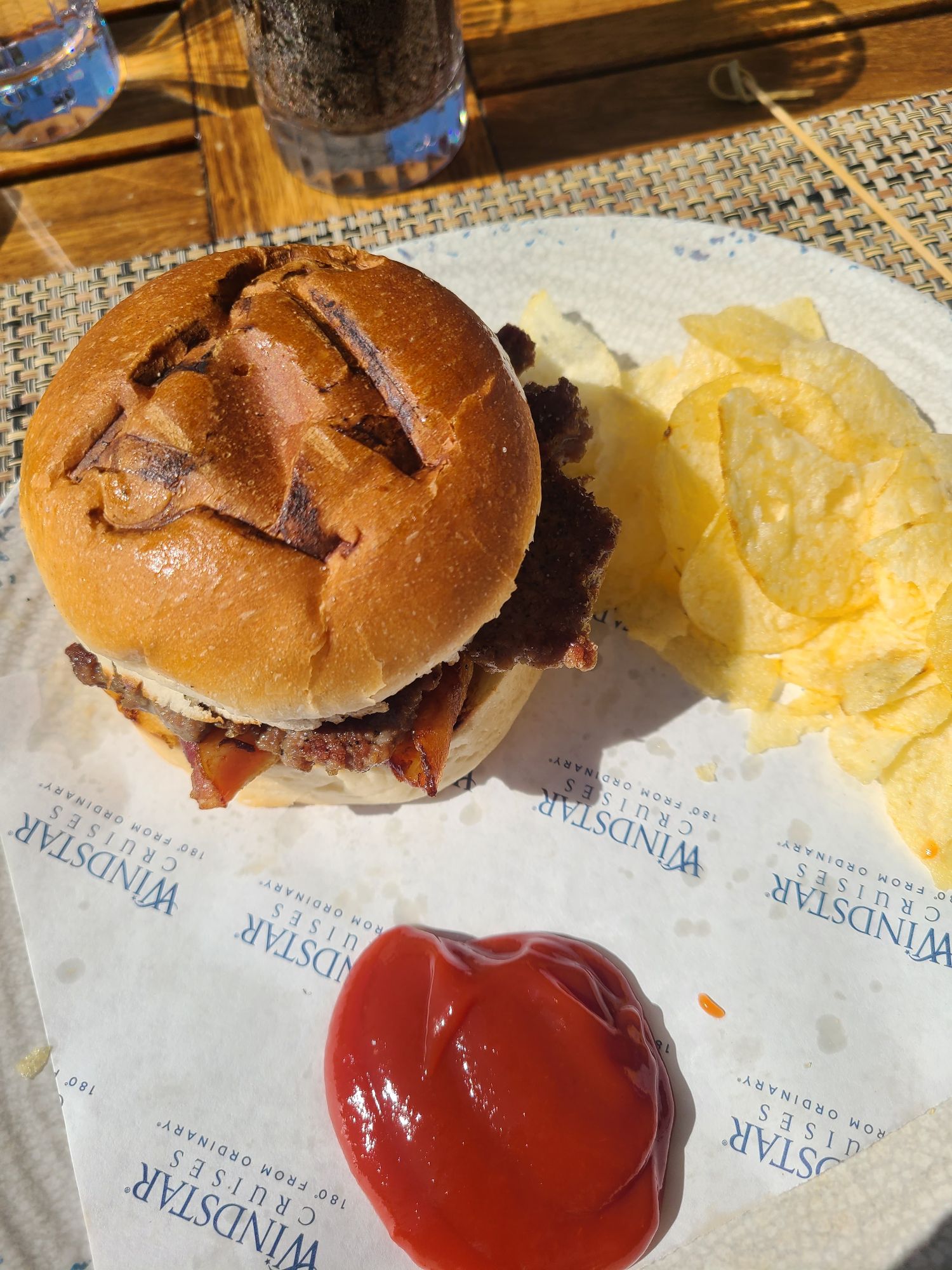 Bacon cheeseburger with golden fries and ketchup on branded paper wrapper at outdoor dining venue