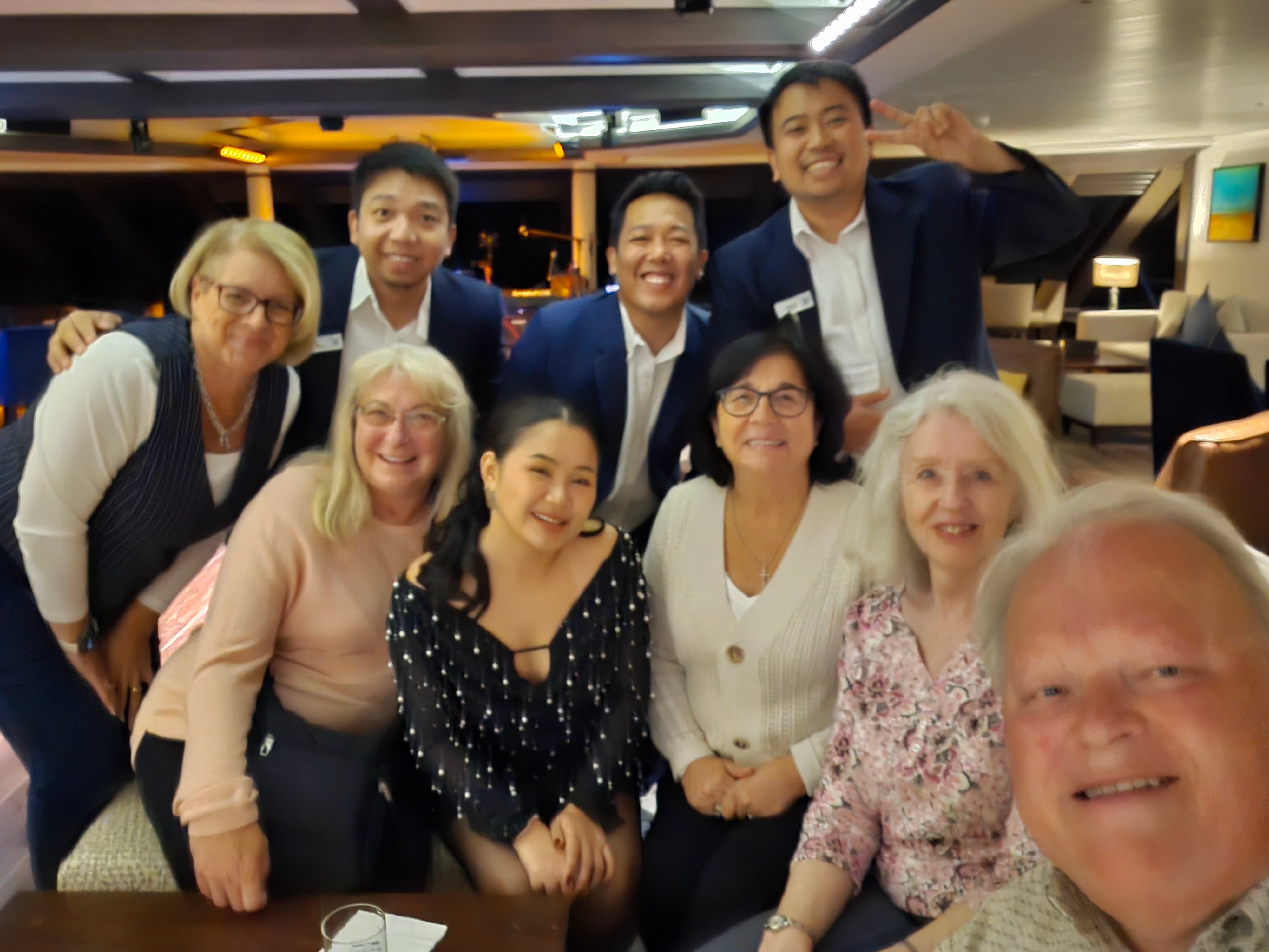 Group of diverse cruise ship staff and passengers smiling together indoors during evening gathering