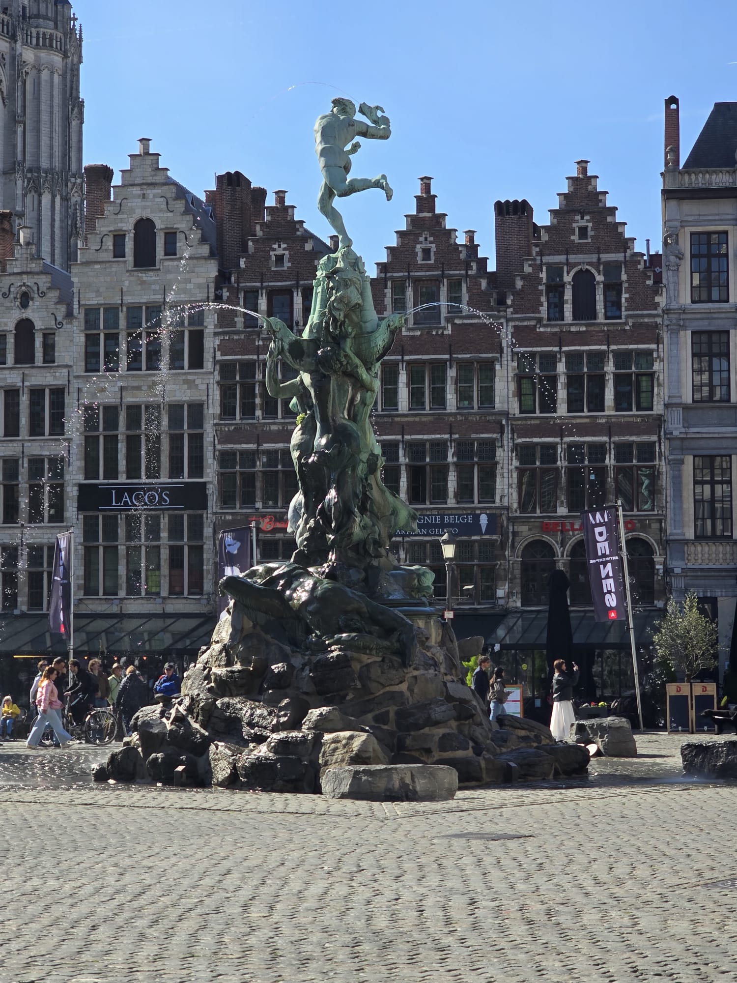 Bronze statue of a leaping cherub figure in a town square fountain with historic buildings behind