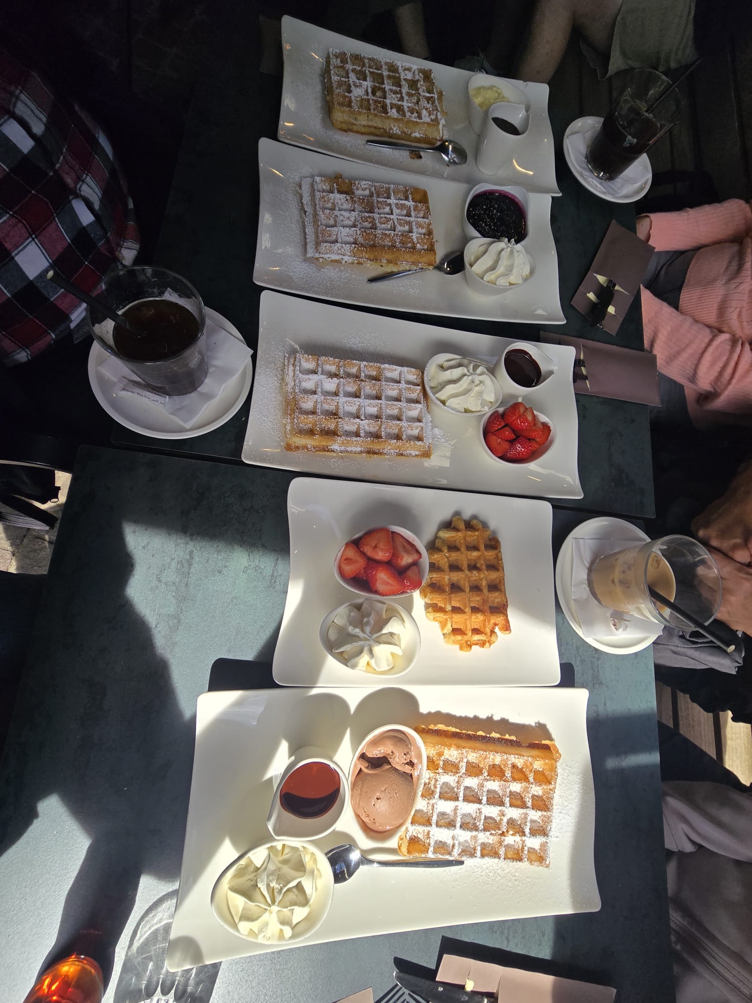 Multiple Belgian waffles dusted with powdered sugar, served with whipped cream and fruit toppings