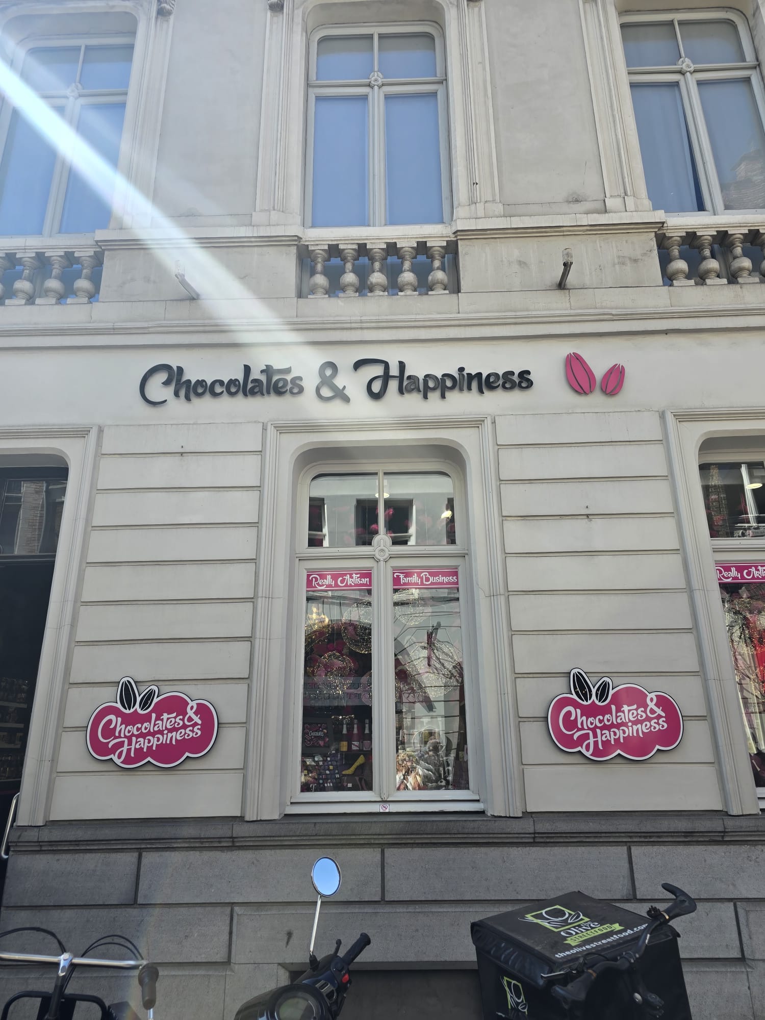 Storefront with 'Chocolates & Happiness' signage and pink cocoa pod logo on white building facade