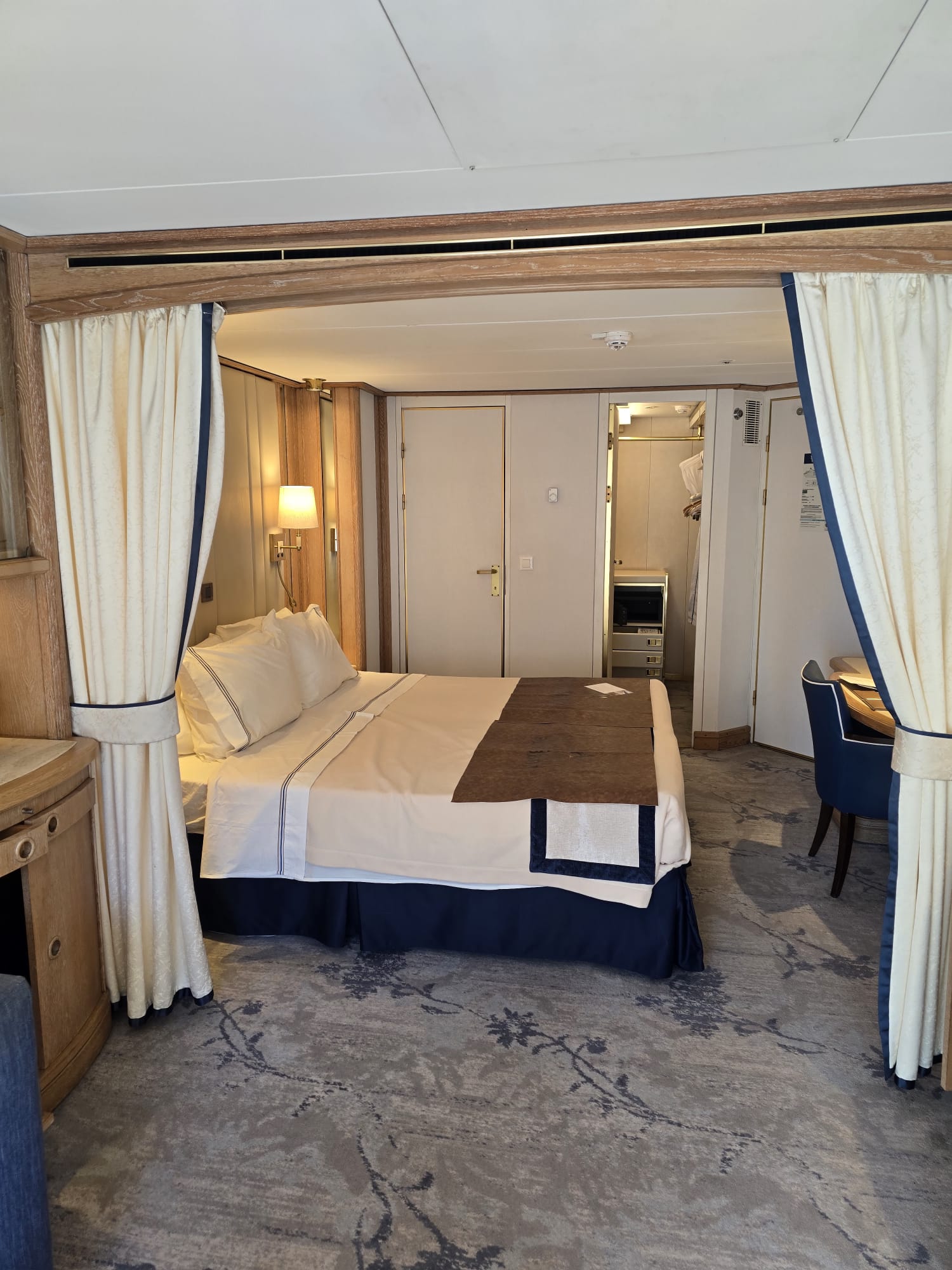 Elegant cruise ship cabin with canopy bed, cream linens, wooden furnishings, and modern bathroom