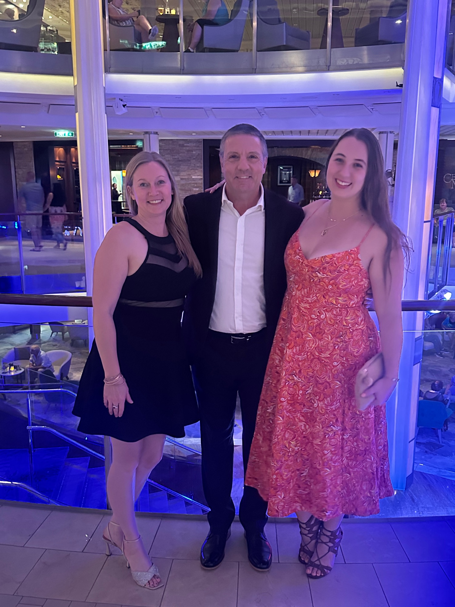Katie Sweetland poses with a man and woman in formal attire inside a modern venue with blue lighting