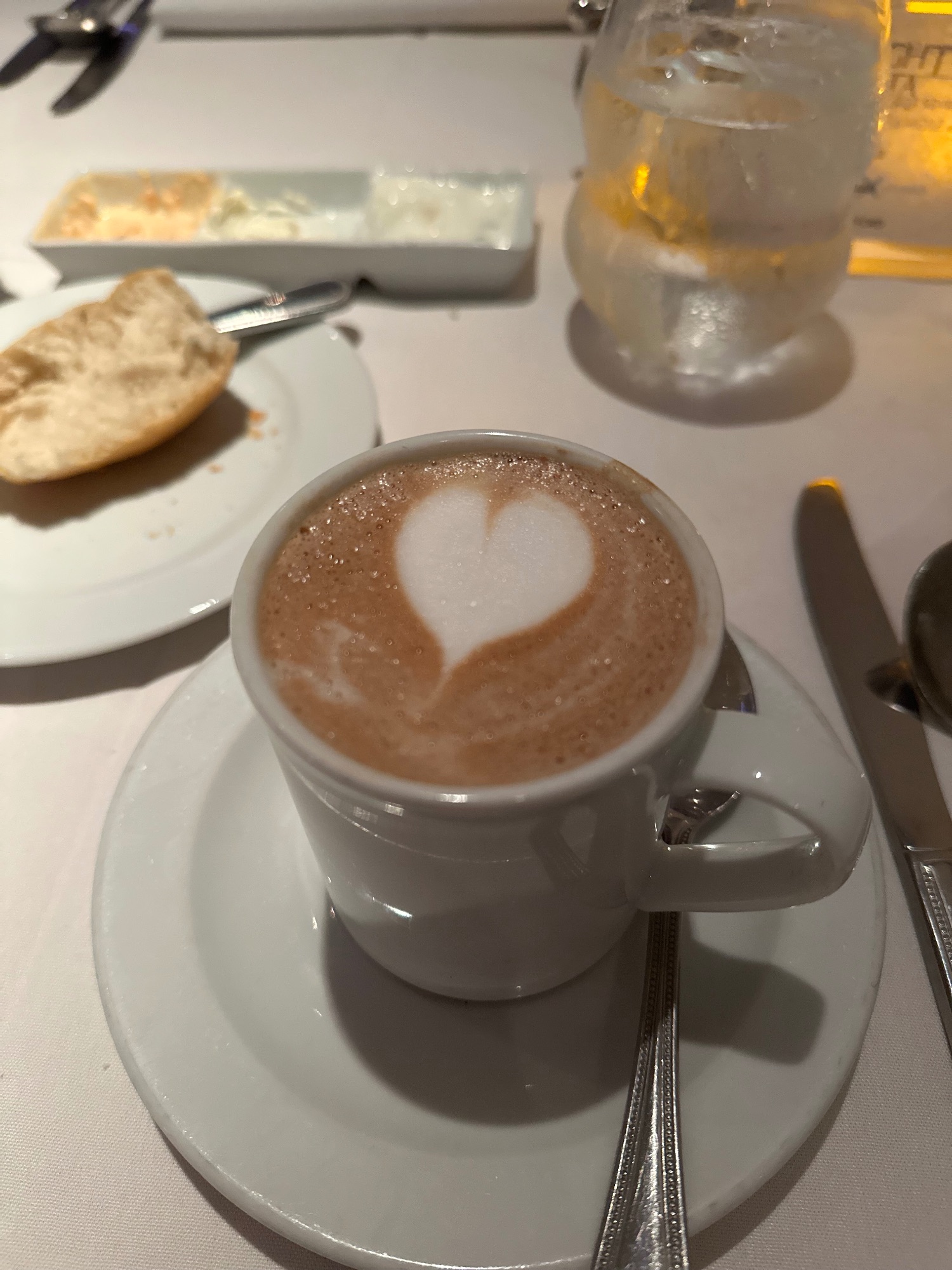 Cappuccino with latte art in a white cup on a saucer with pastry and glass of water at a café