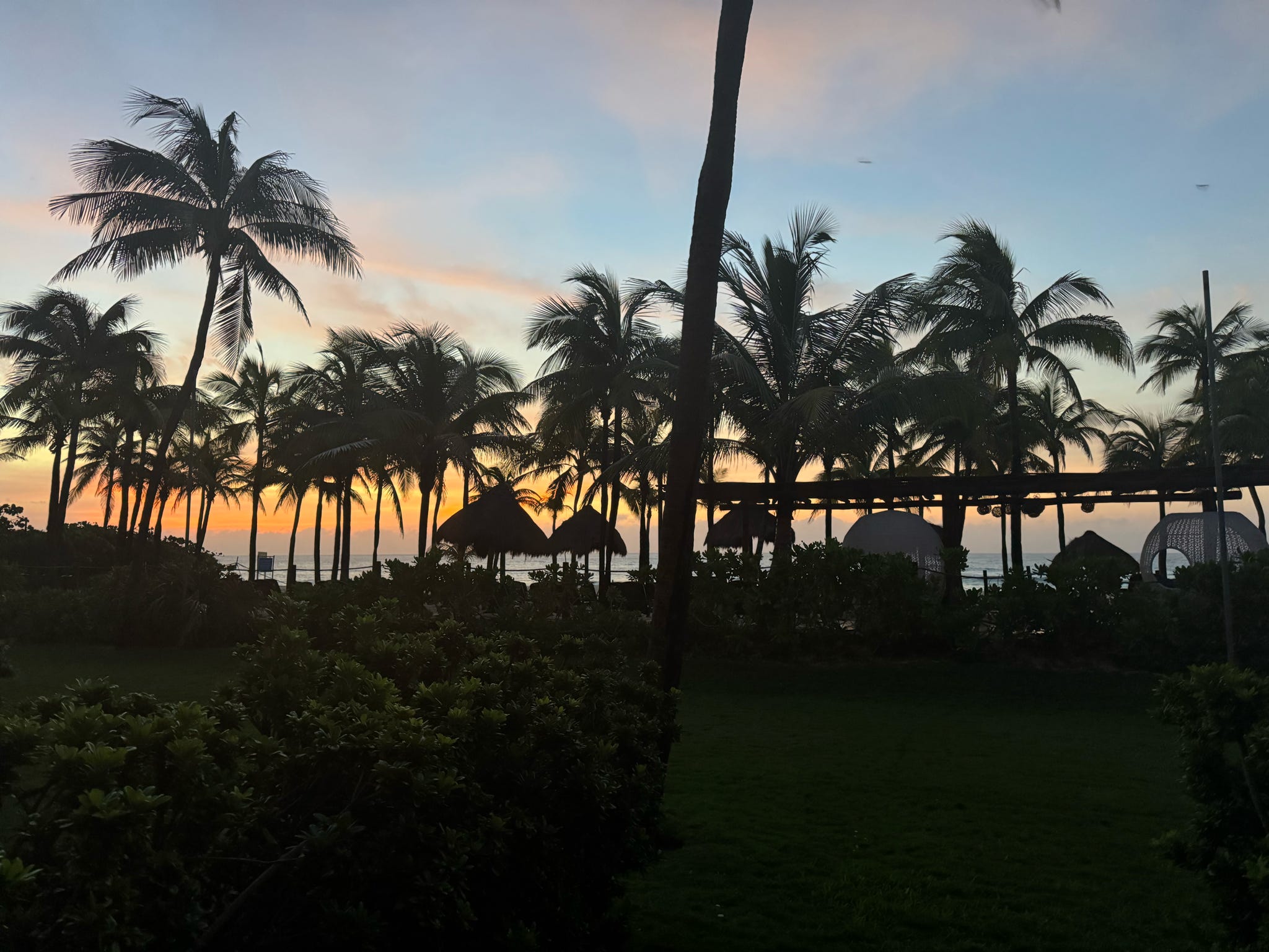 Silhouetted palm trees frame a vivid golden sunset over a tropical beach resort.