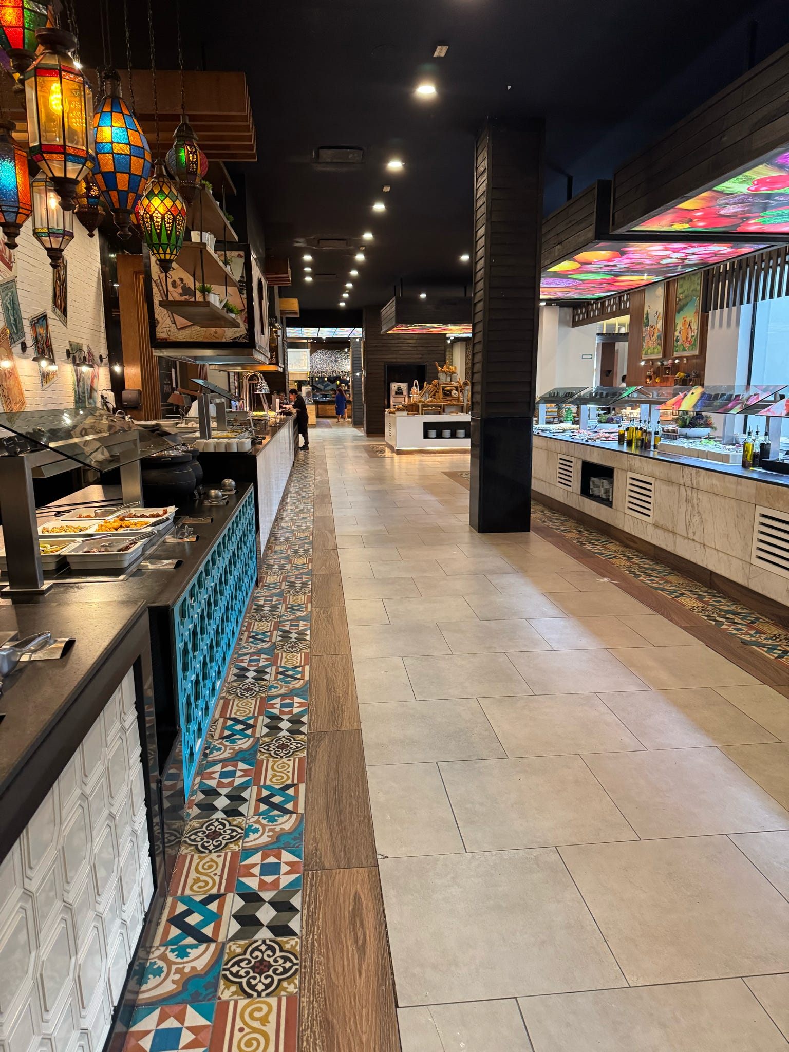 A vibrant resort buffet corridor with Moroccan lanterns and intricate mosaic floor tiles.