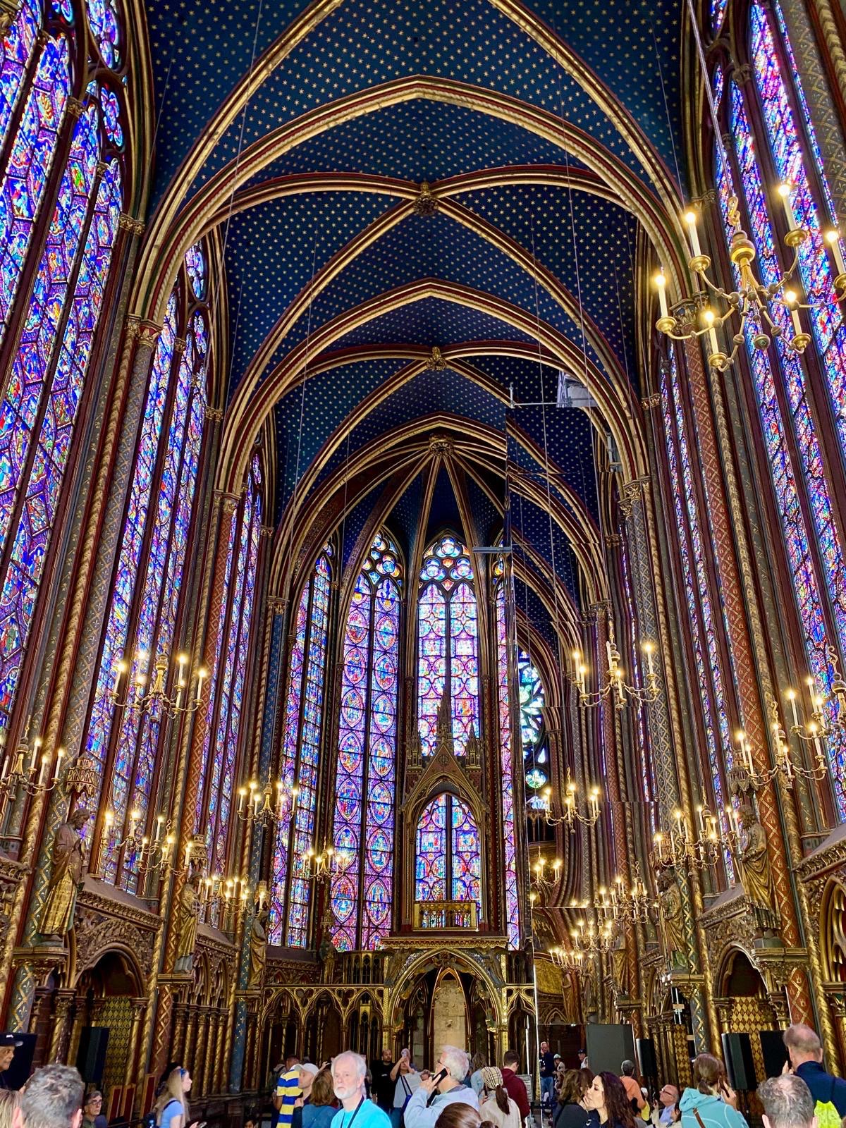 Interior of a Gothic cathedral with soaring blue ceiling, golden arches, and vibrant stained glass windows