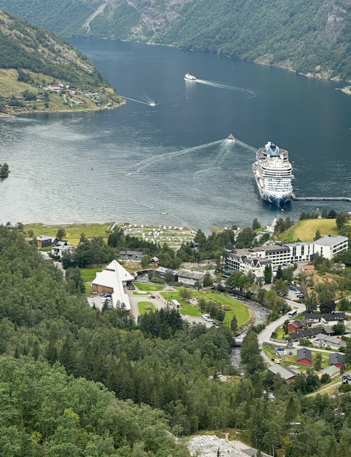 Large cruise ship anchored in a deep Norwegian fjord with dramatic cliff walls and a small settlement below
