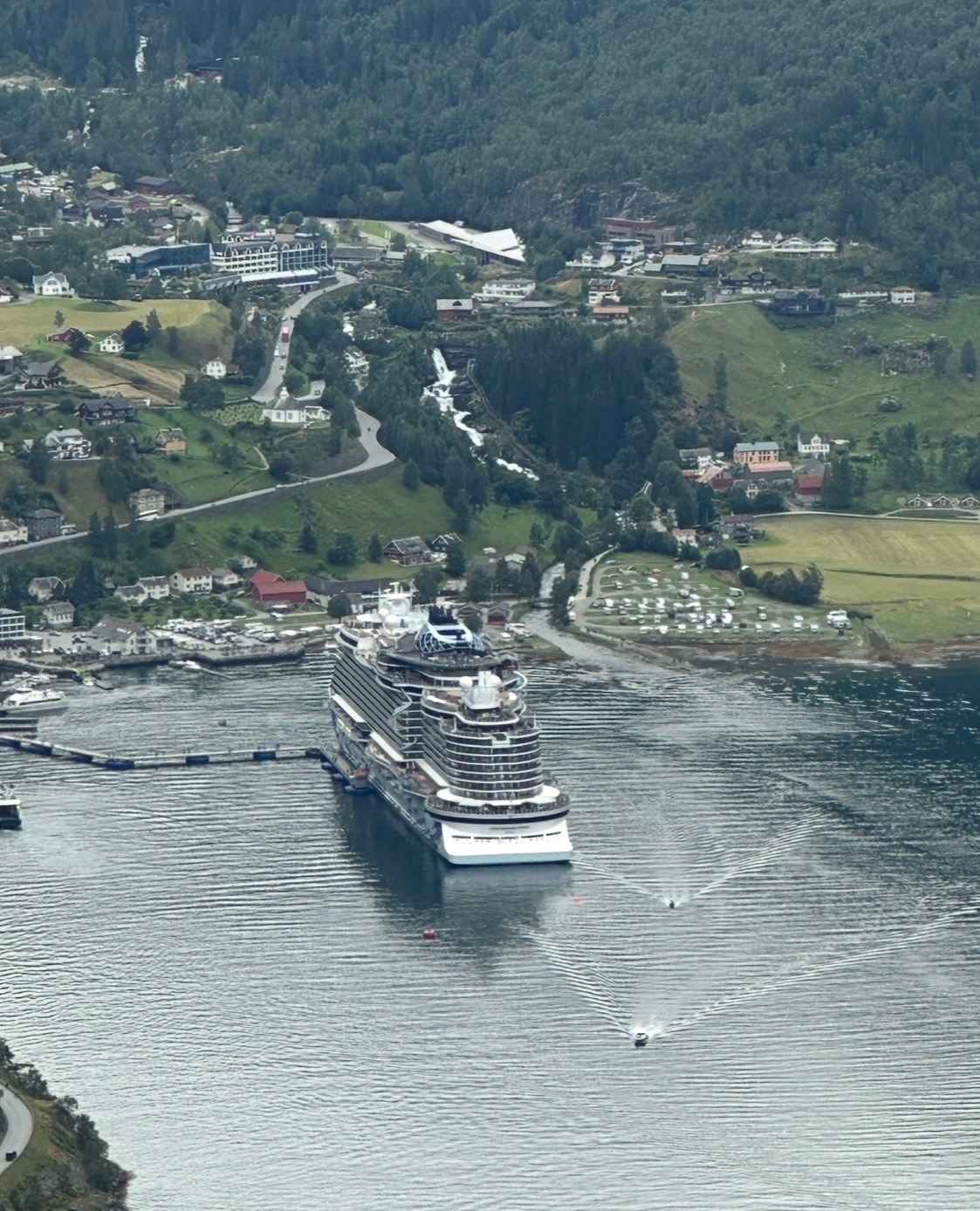 Panoramic view of a deep blue fjord surrounded by steep forested mountains with a small cruise ship visible