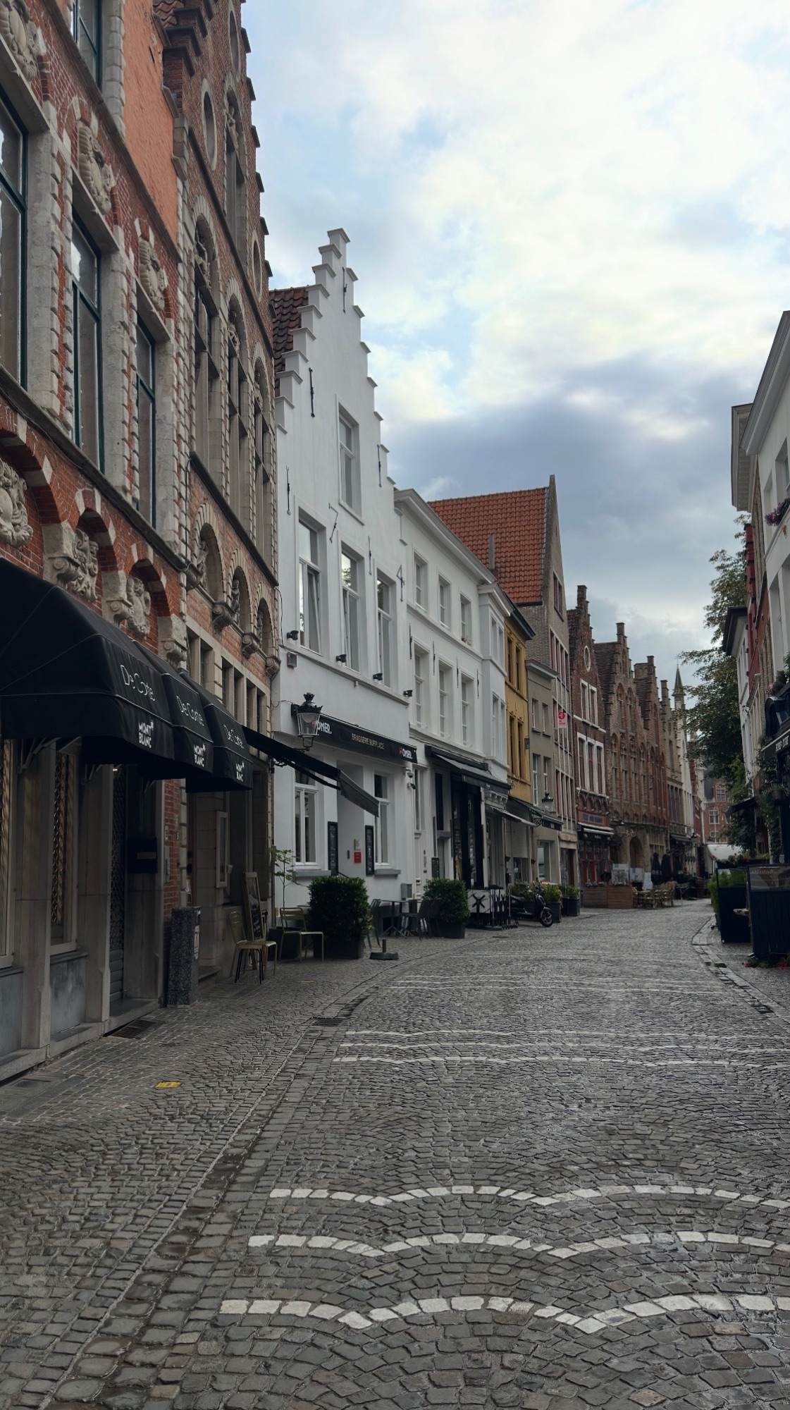 Charming European street with historic brick buildings, outdoor café seating, and pedestrians in a town square