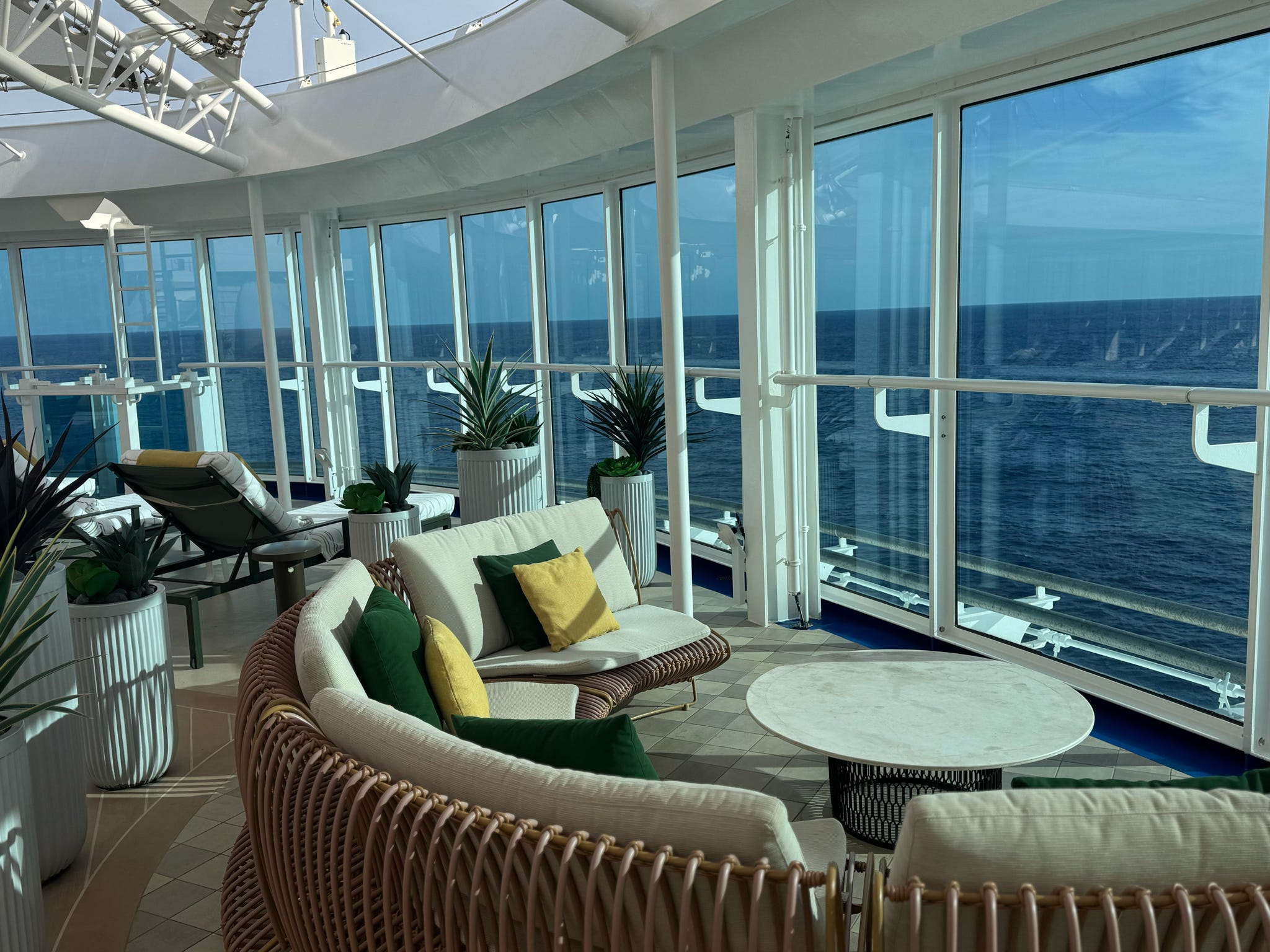 A luxurious cruise ship lounge with wicker furniture and sweeping panoramic ocean views.