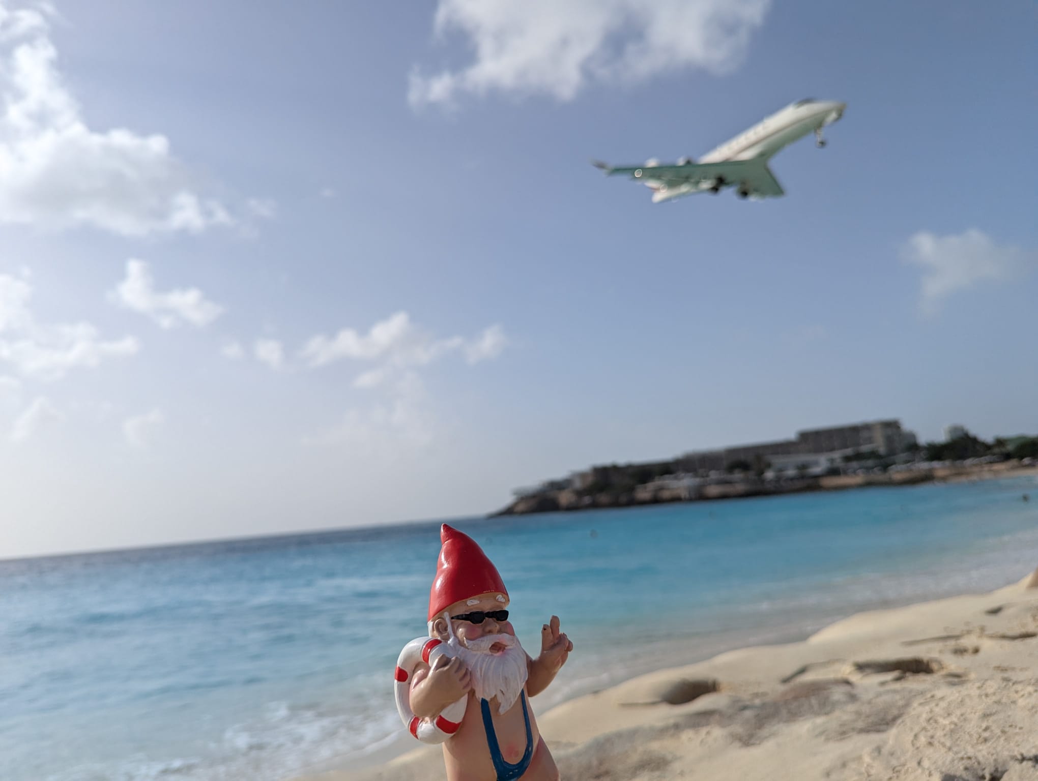 A cheeky beach gnome poses on Maho Beach as a jet makes its iconic low-altitude approach overhead.