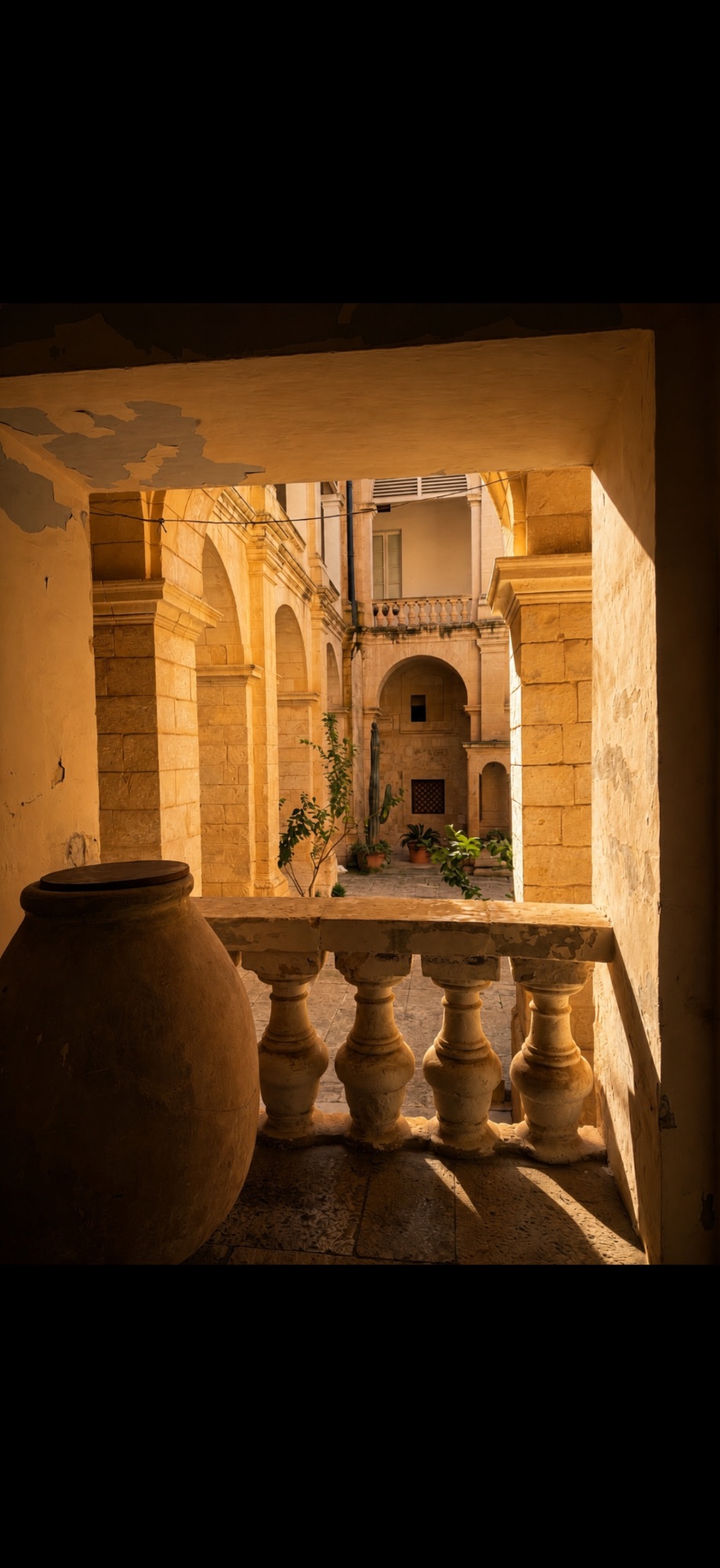 Interior courtyard view through a balcony with ornate stone railings overlooking traditional Maltese architecture
