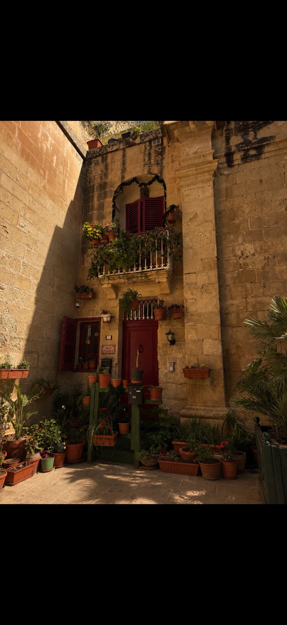 Terracotta-potted traditional Maltese townhouse facade with red wooden doors and wrought-iron balconies
