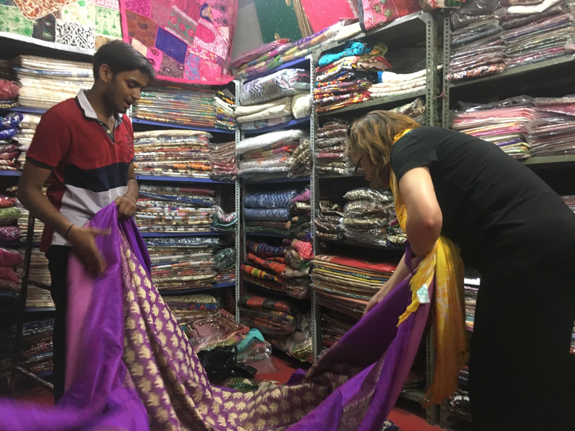 A shopkeeper in India displays colorful purple and gold fabric to Michelle Whalen in a textile market stall