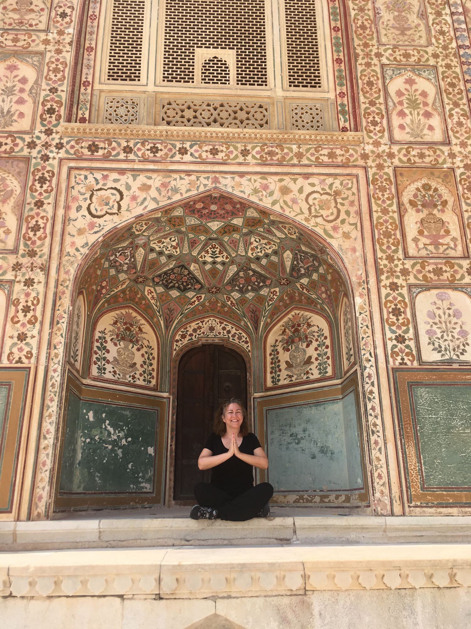 Michelle Whalen sits cross-legged in a yoga pose in front of an ornate arched doorway with intricate floral inlay patterns