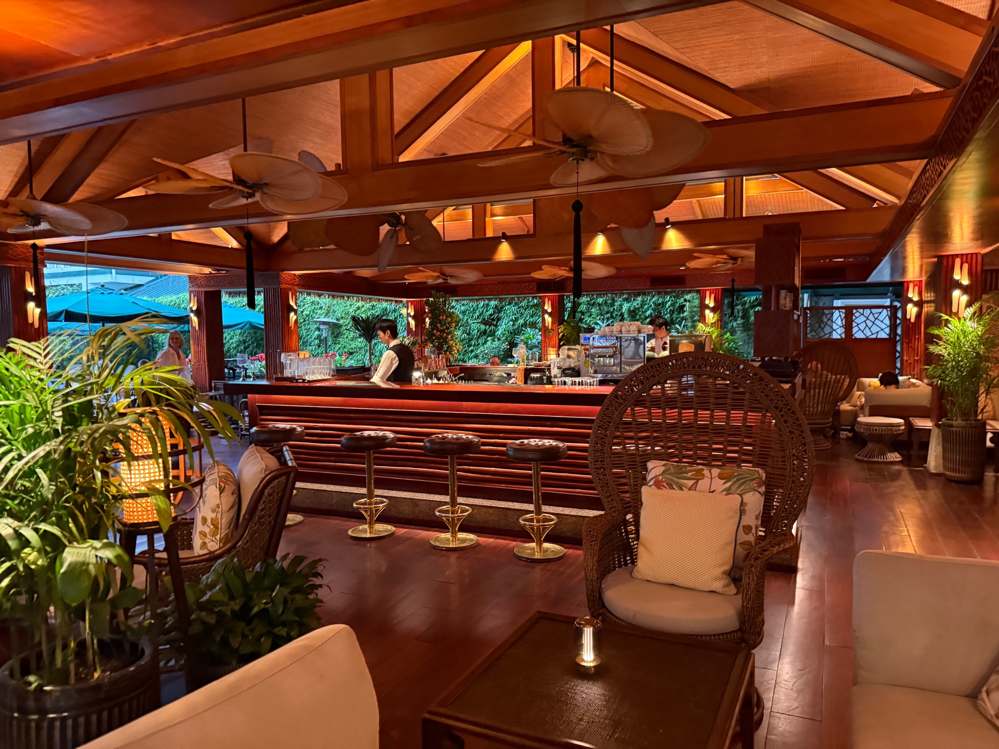 Interior bar and lounge space with wooden beams, rattan chairs, and ocean views through windows