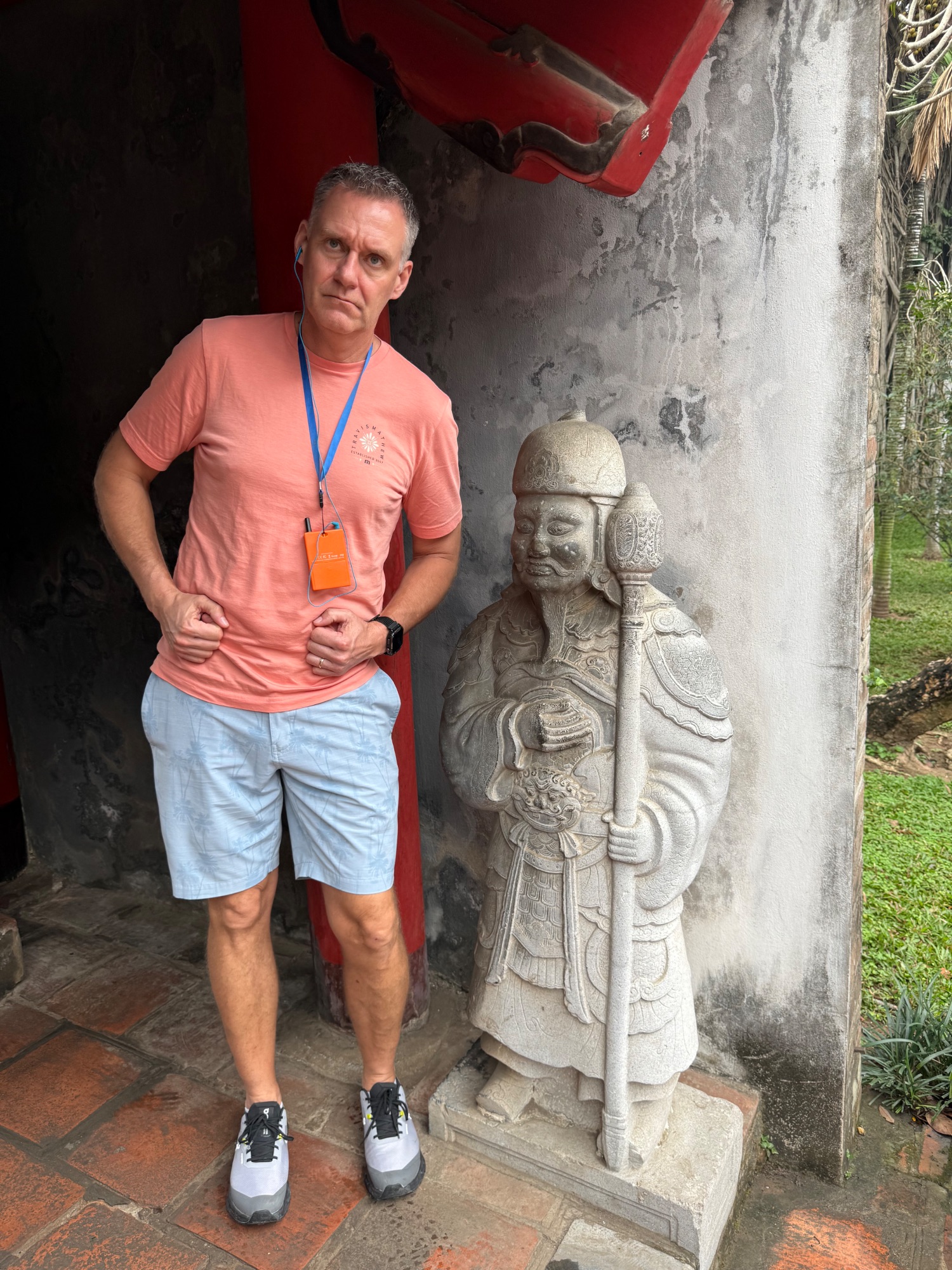 Man in coral shirt posing beside carved stone statue of a Vietnamese warrior or deity