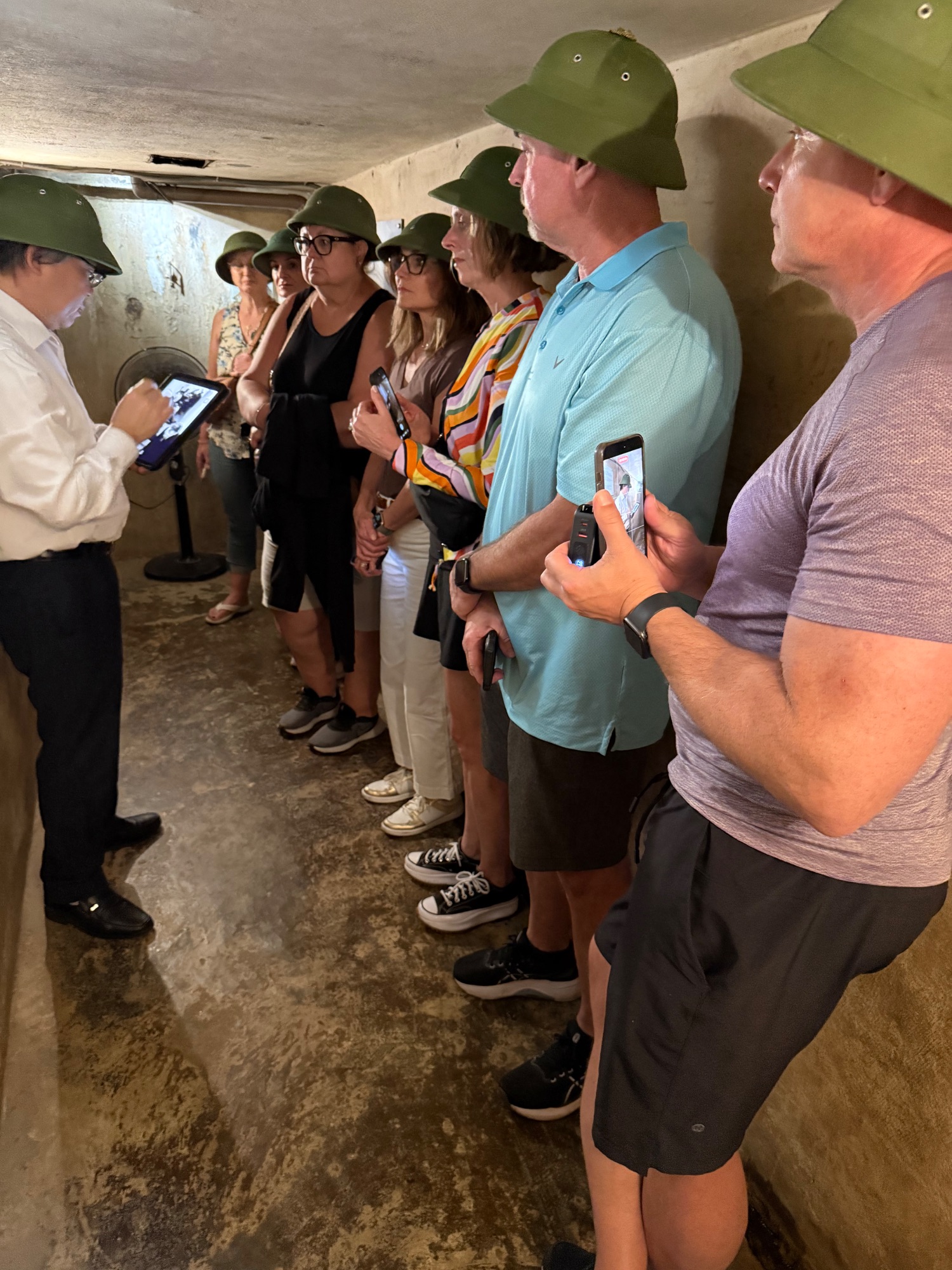 Tour group wearing military-style helmets inside a concrete underground tunnel or bunker