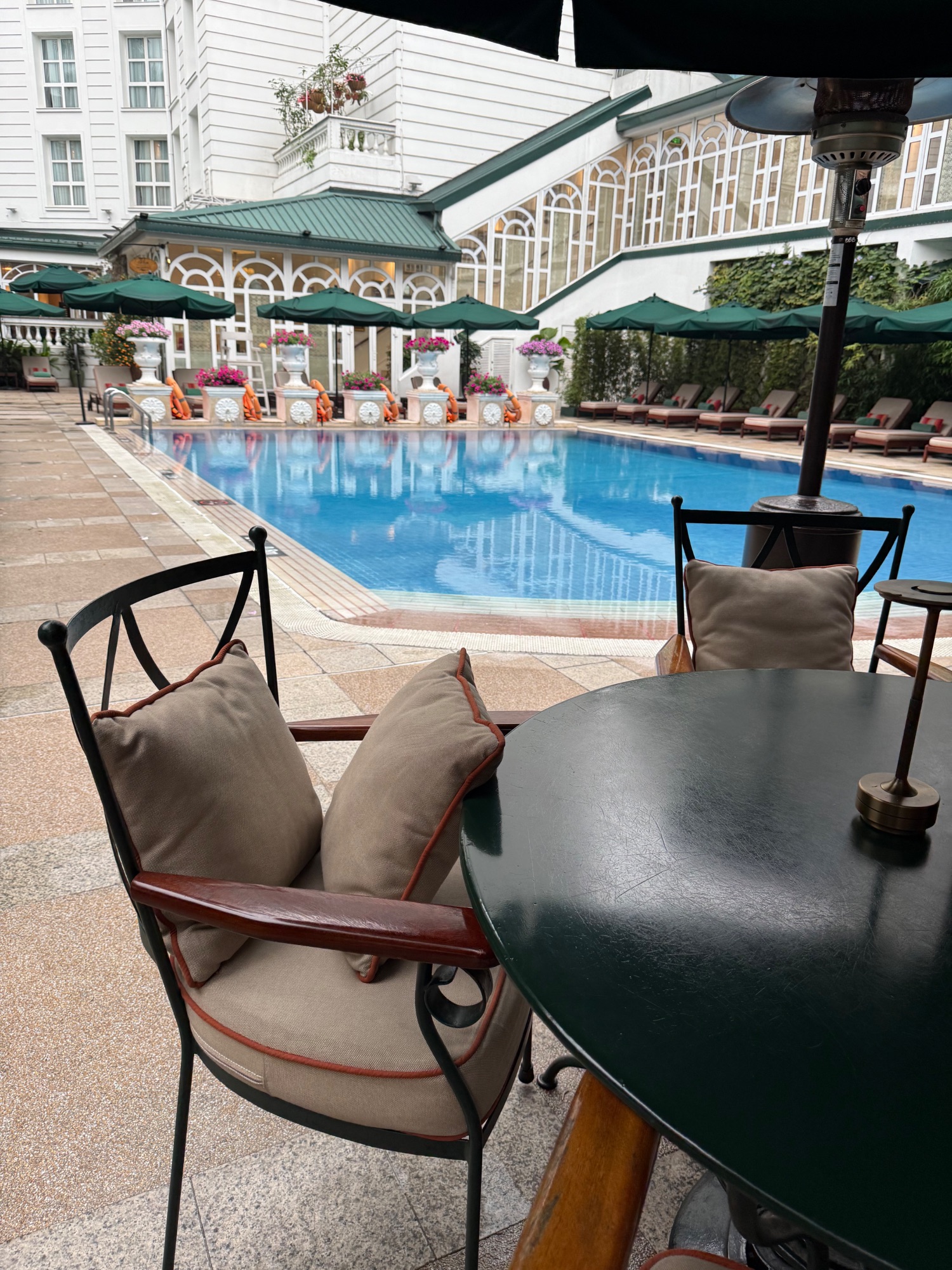 Elegant poolside lounge area with green umbrellas, cushioned seating, and manicured landscaping
