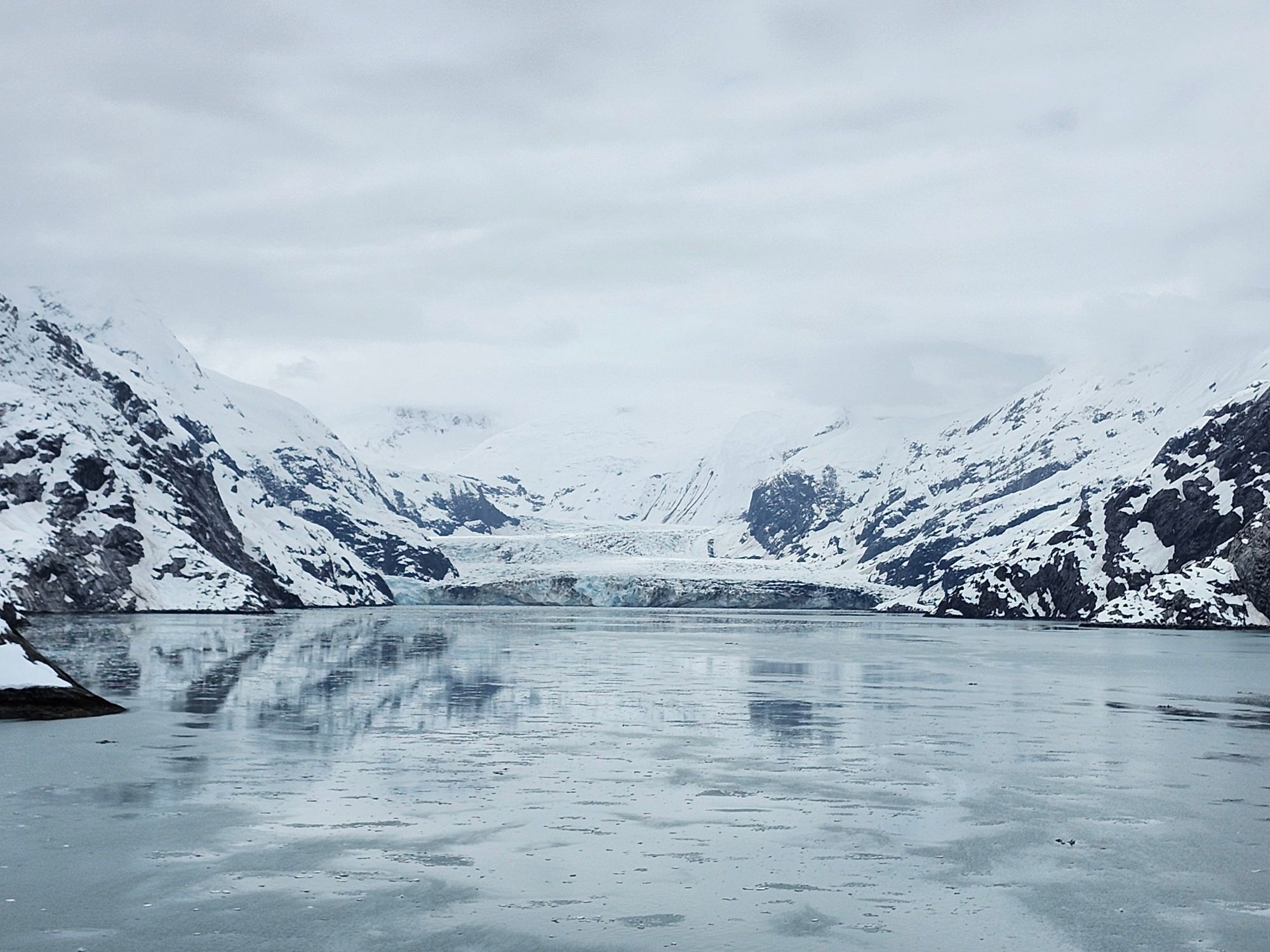 Frozen glacier and icy landscape reflected in still water between snow-covered mountain slopes