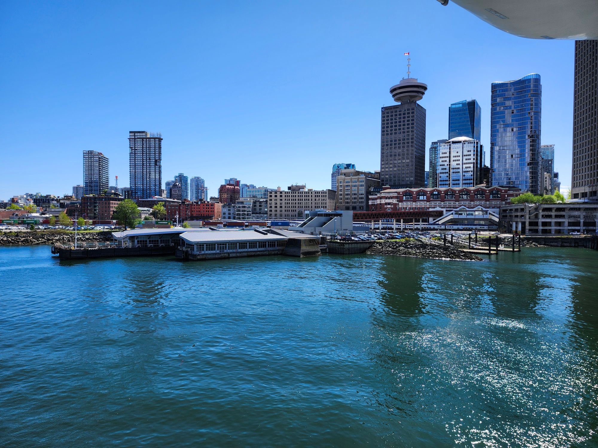 Vancouver skyline with Harbour Centre tower viewed from water, modern high-rises against blue sky