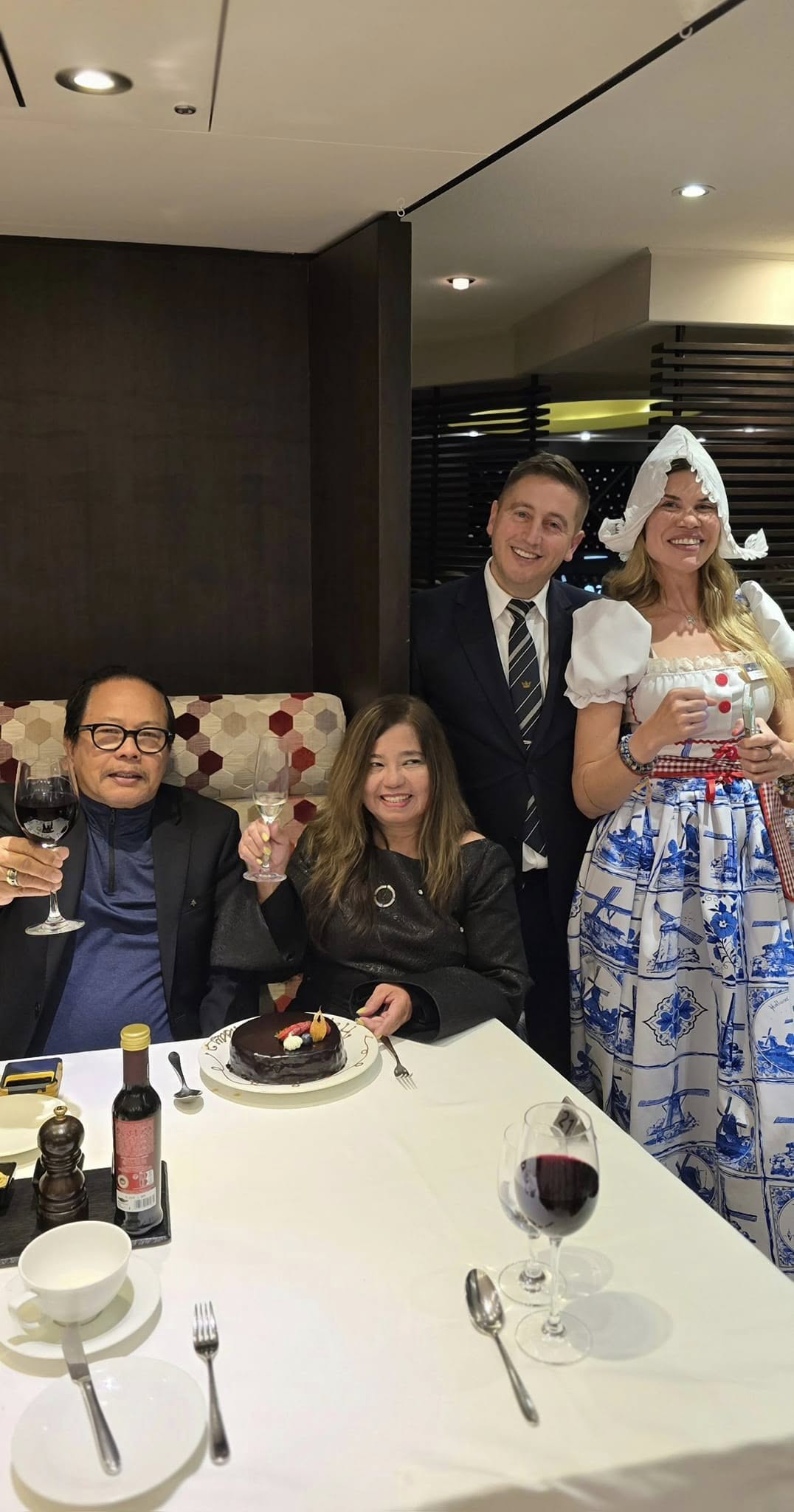 Four people toasting with wine and cake at an elegant indoor dinner celebration