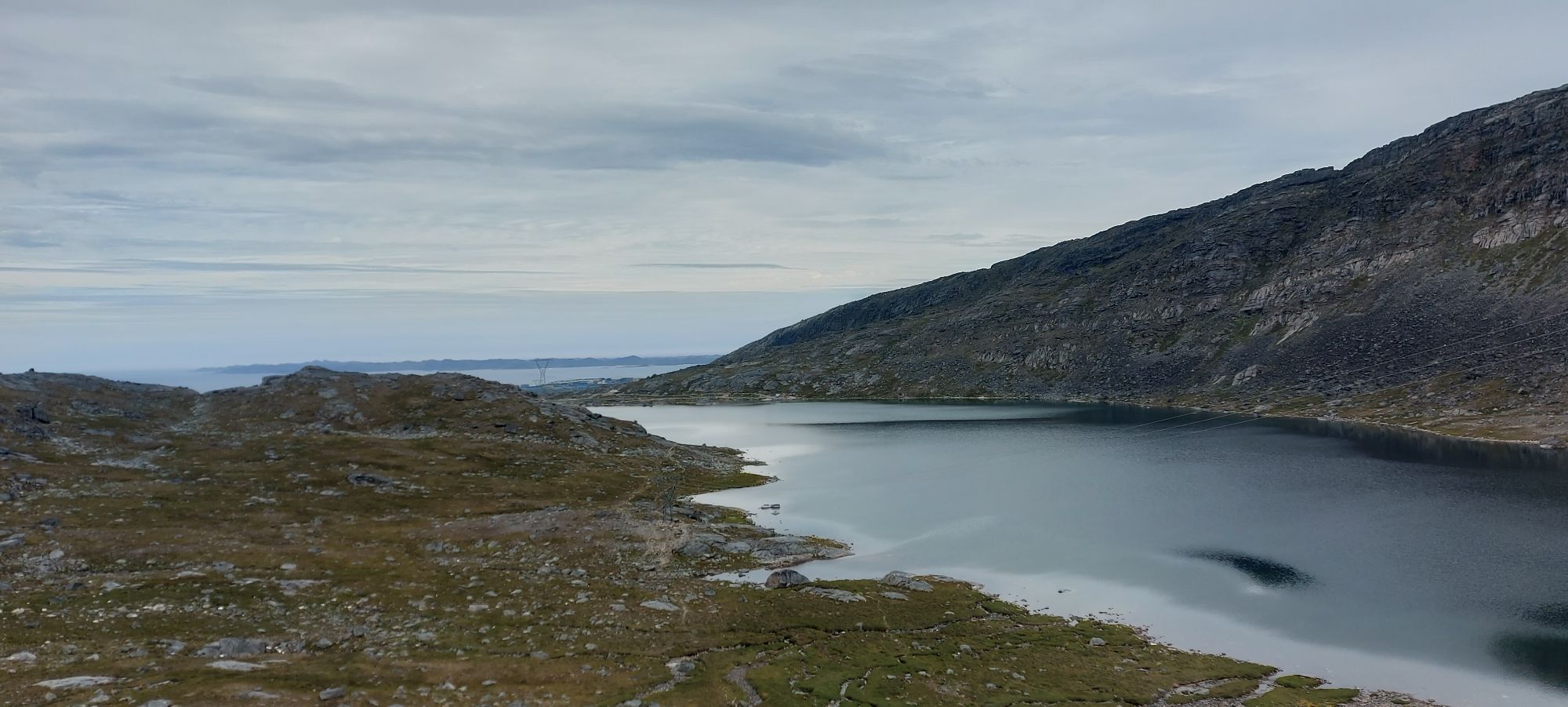 Serene alpine lake reflecting surrounding mountains with sparse vegetation and rocky terrain under overcast sky