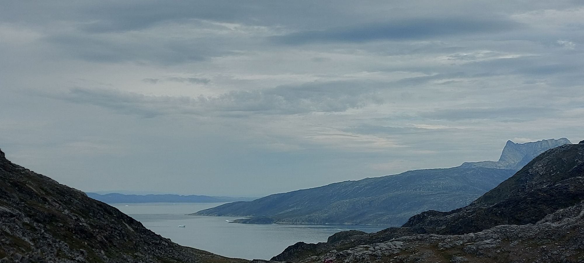 Couple hiking on rocky tundra with distant fjord, mountains, and sea visible across the landscape