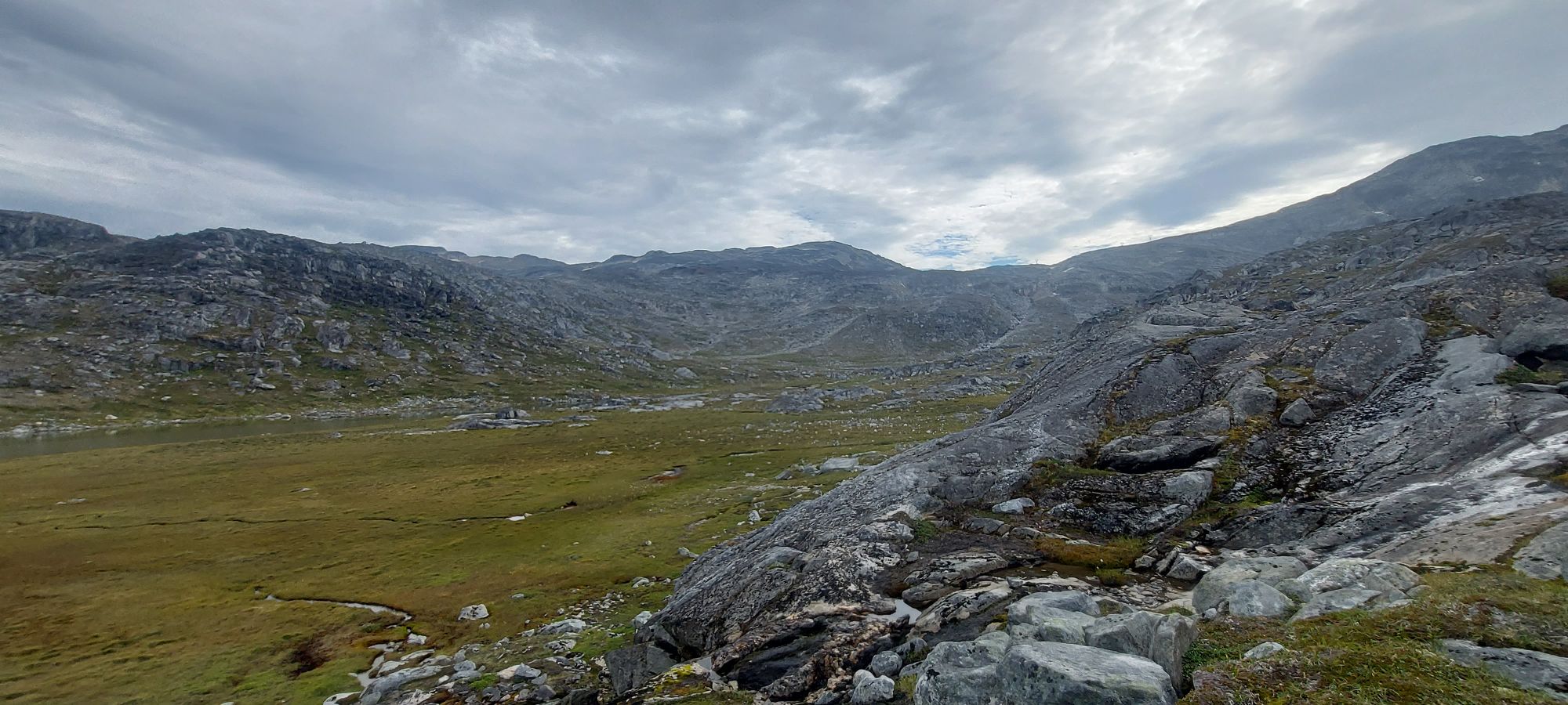 Panoramic view of turquoise fjord with snow-capped mountain peak across the water and rocky shoreline