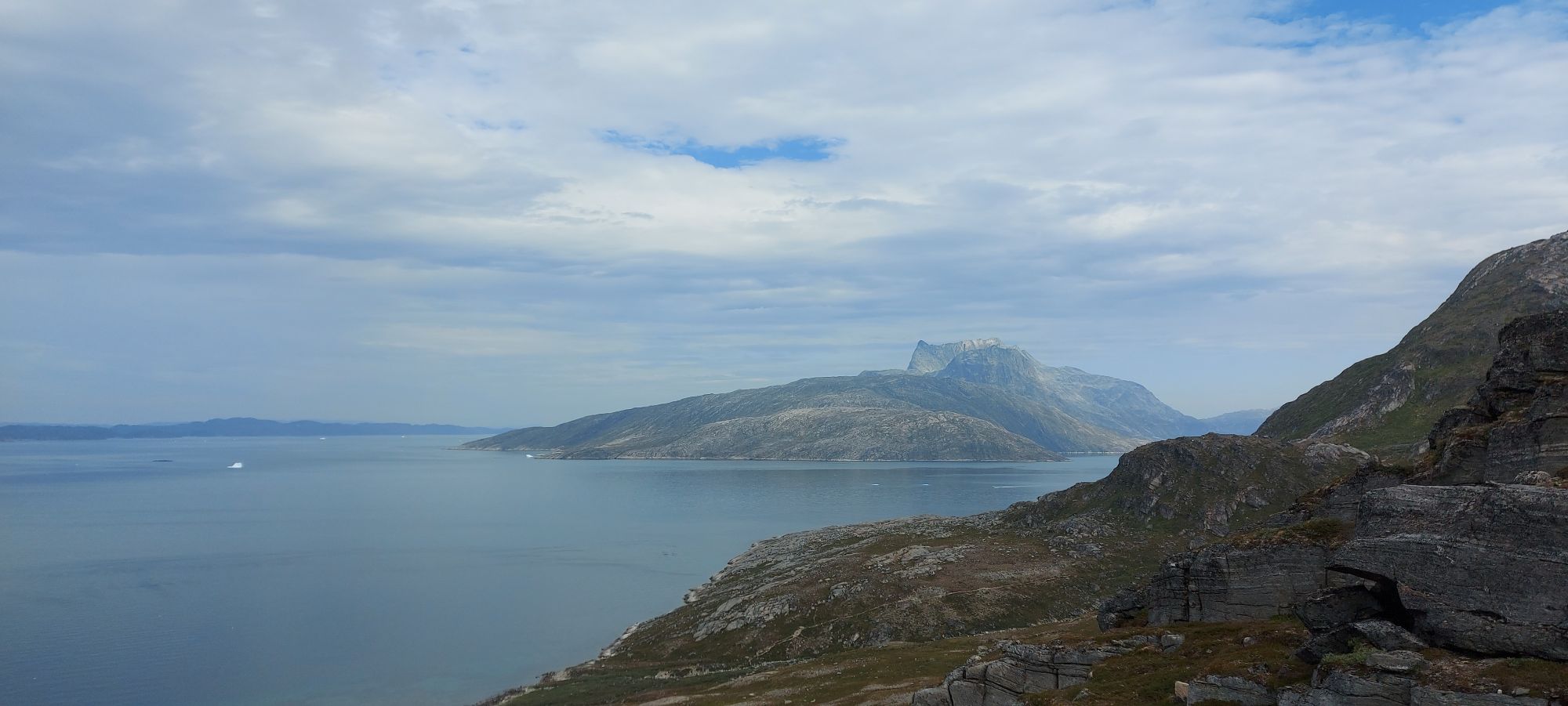 Woman smiling on rocky overlook with turquoise fjord, mountains, and small island visible in background