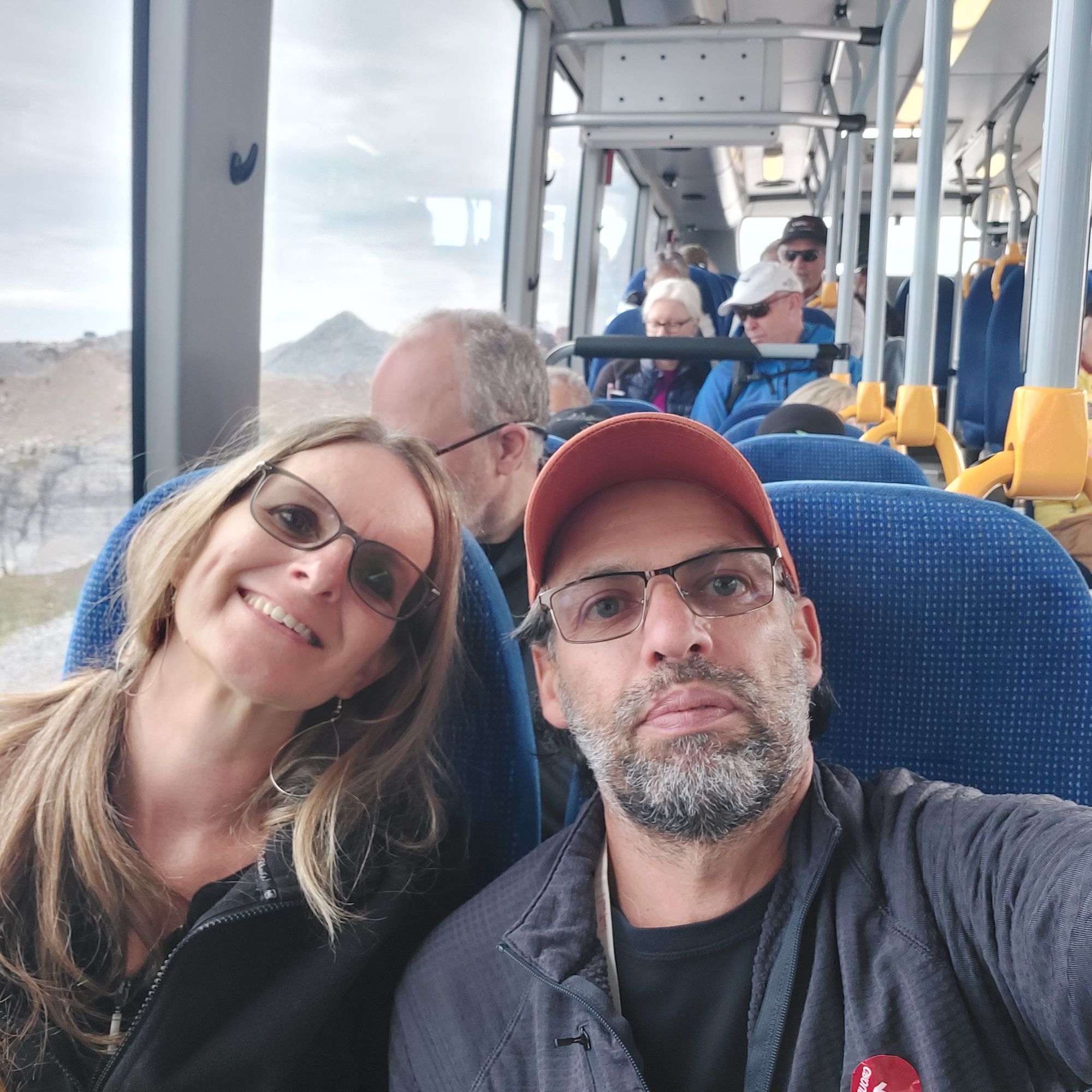 Couple on bus interior with mountain landscape visible through window during Greenland excursion